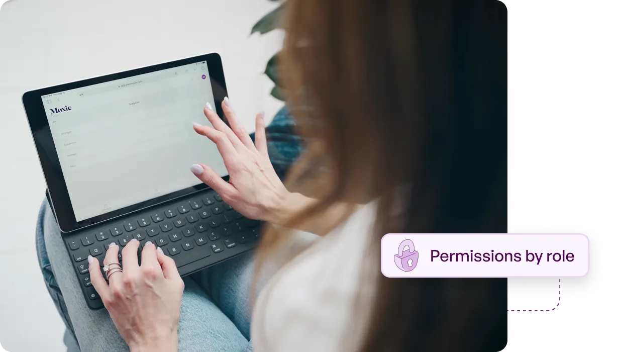Person using a tablet with keyboard displaying a webpage titled 'Moxie' and an overlay text box saying 'Permissions by role'.