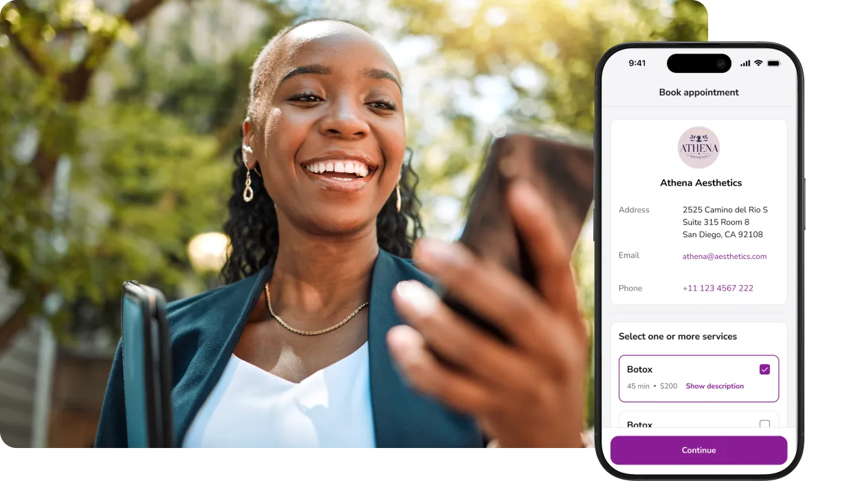Smiling woman holding a phone with an online appointment booking app for Athena Aesthetics displayed on screen.