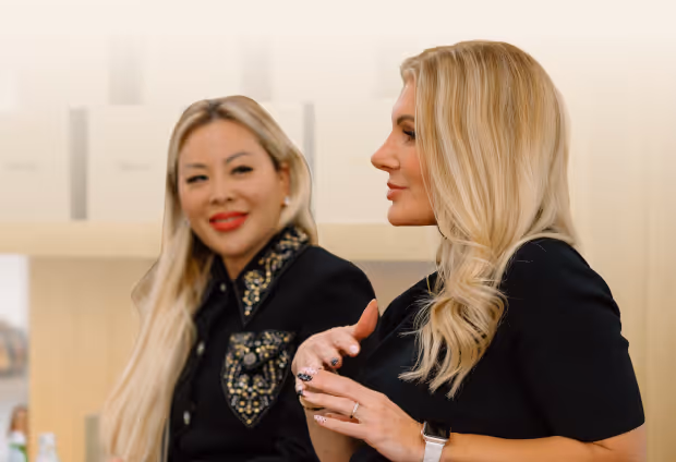 Two women with long blonde hair engaged in conversation, one gesturing with her hands.