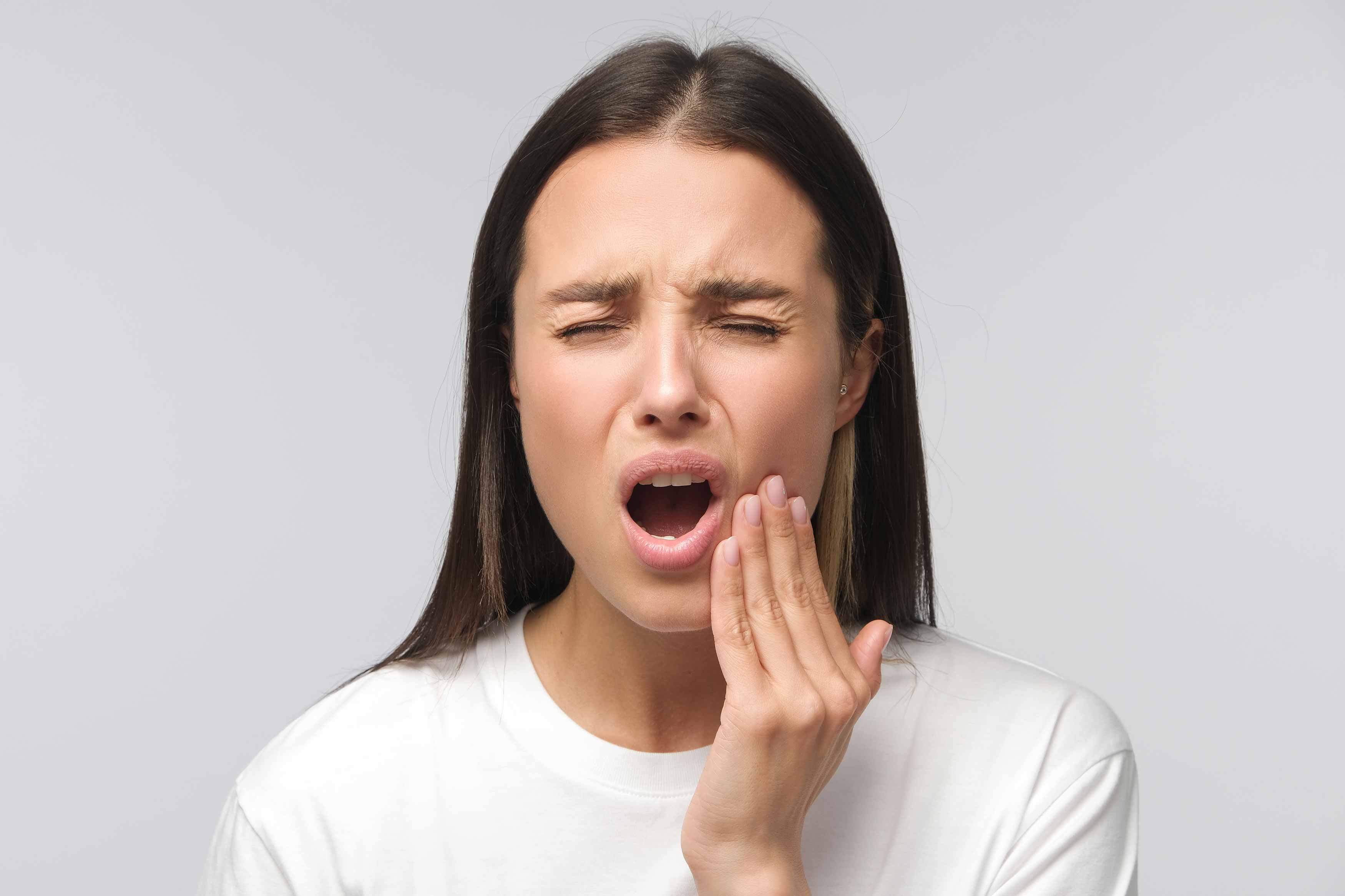 Young female feeling toothache pain in the lower molar. She is holding her lower left jaw in discomfort