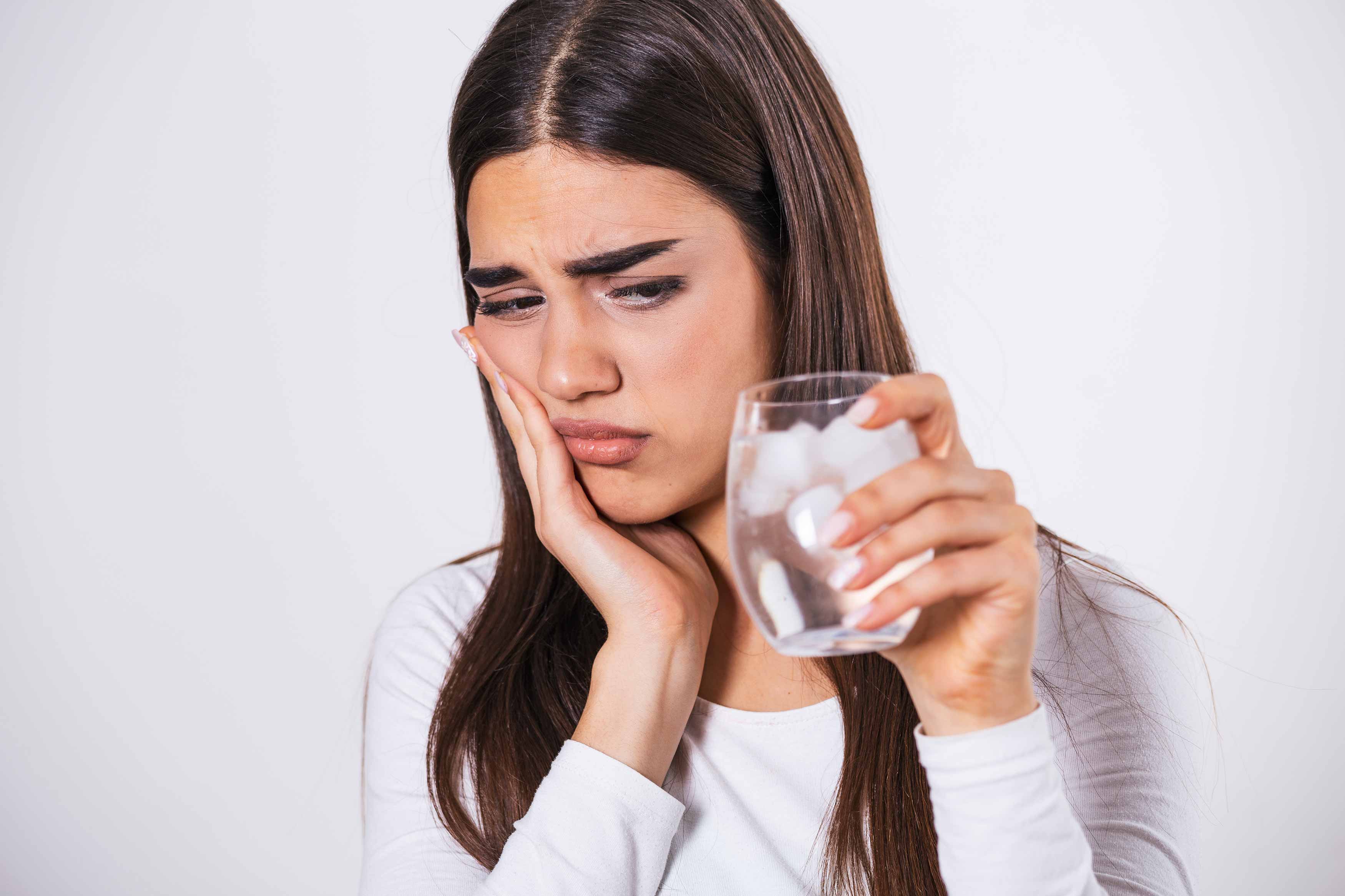 Young female having strong toothache pain after drinking a glass of iced water