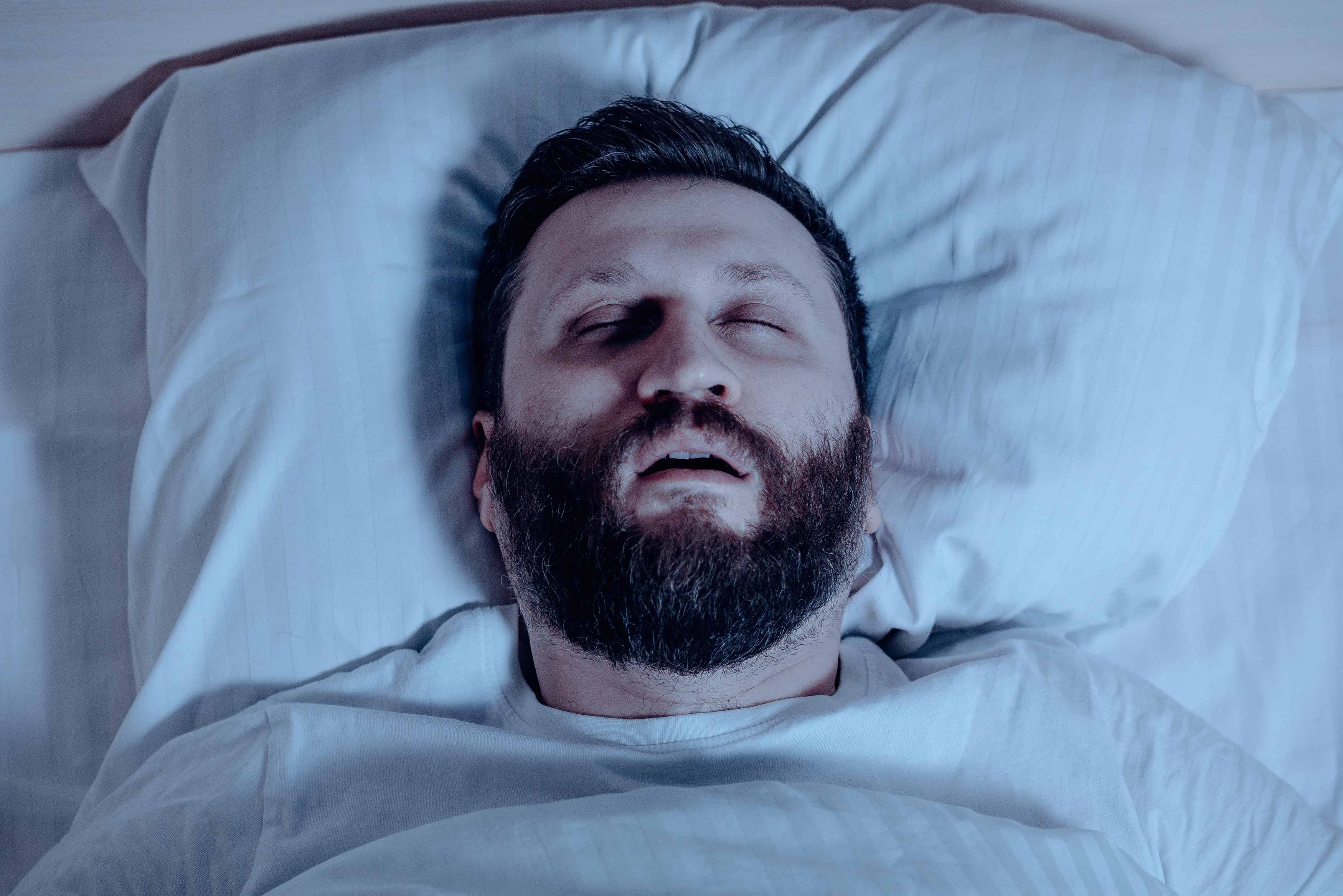 Middle aged man sleeping in his bed with his mouth open and snoring. 