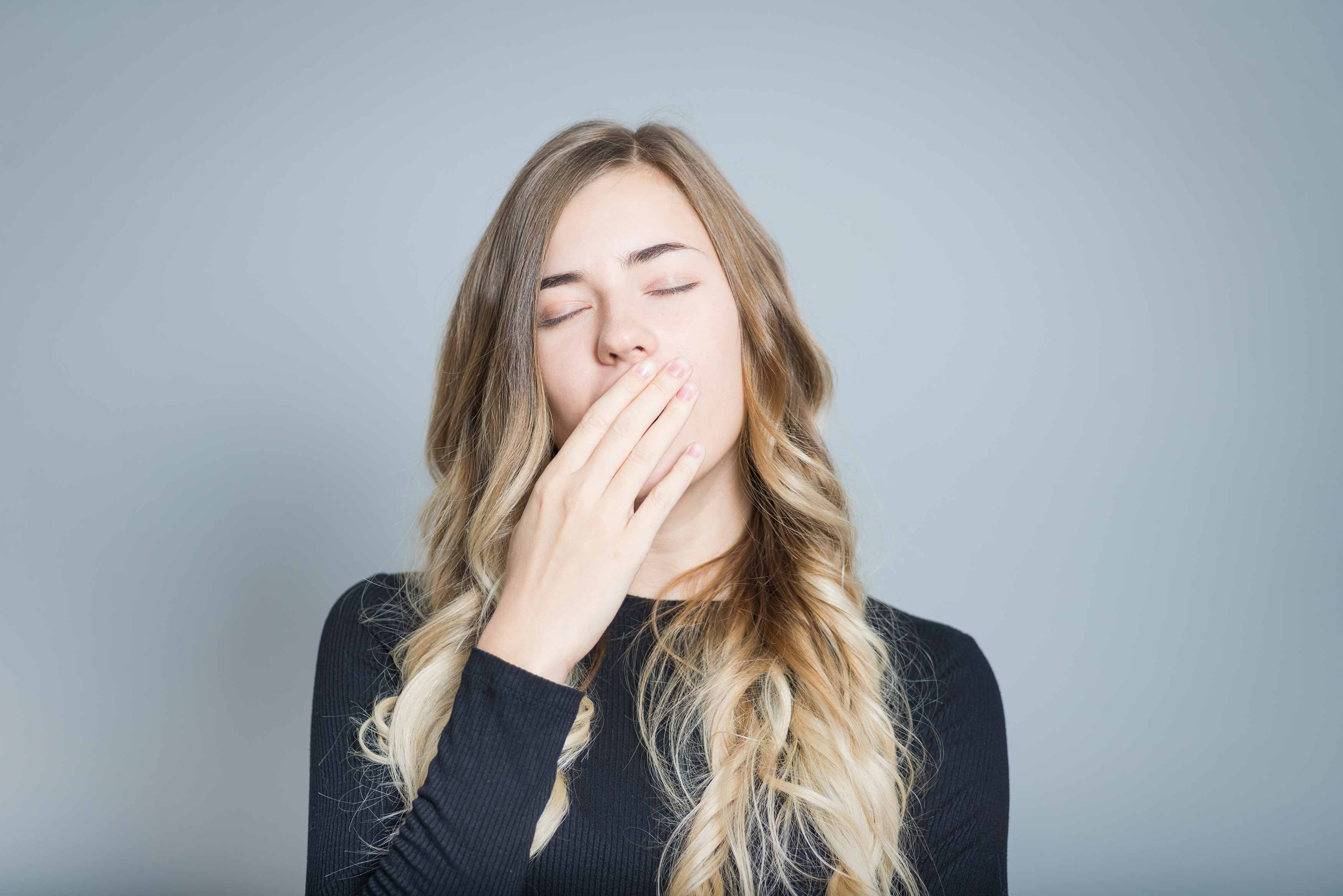 Young female covering her yawn as she is sleepy 