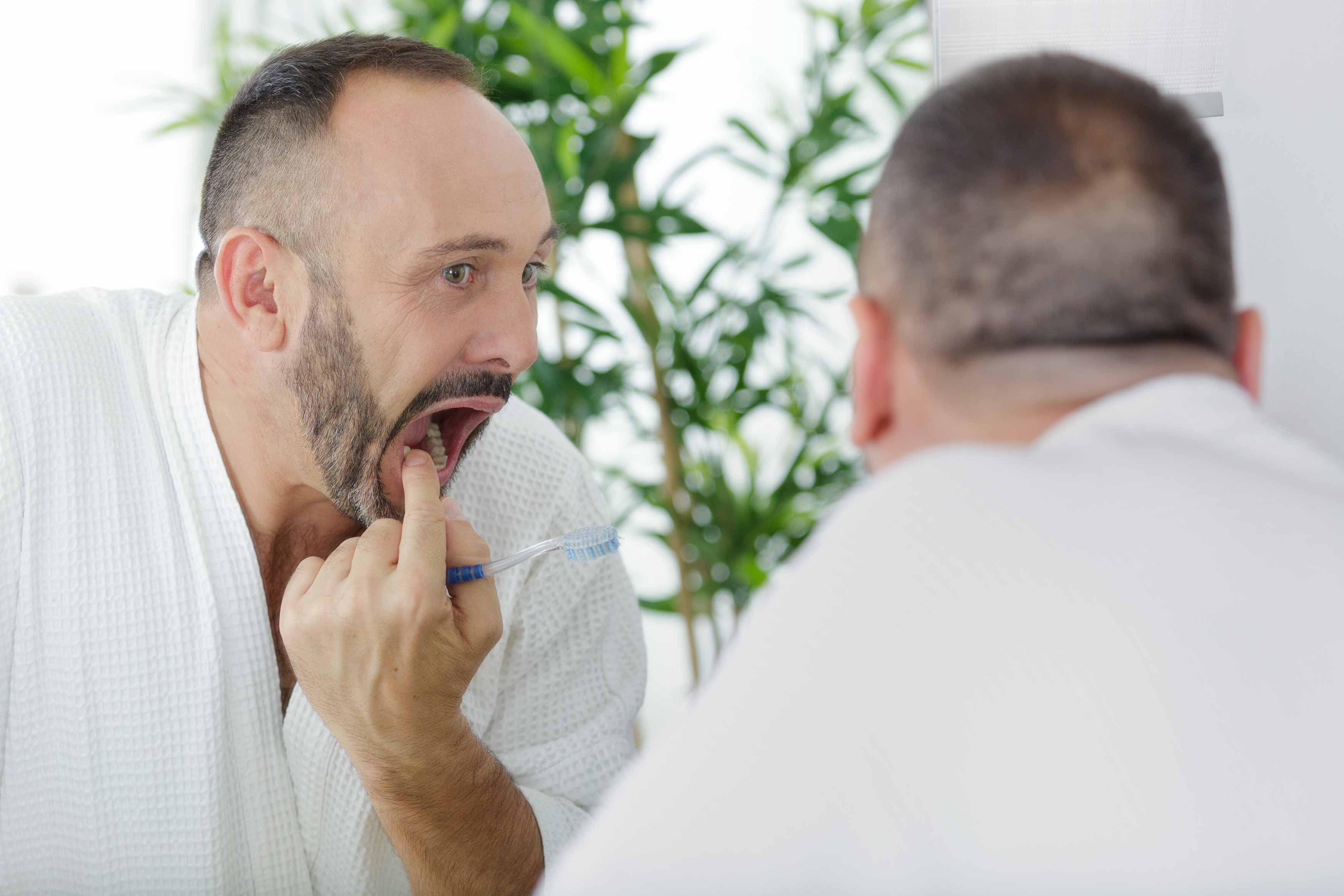 a photo of a man looking into a mirror wriggling his loose lower right tooth