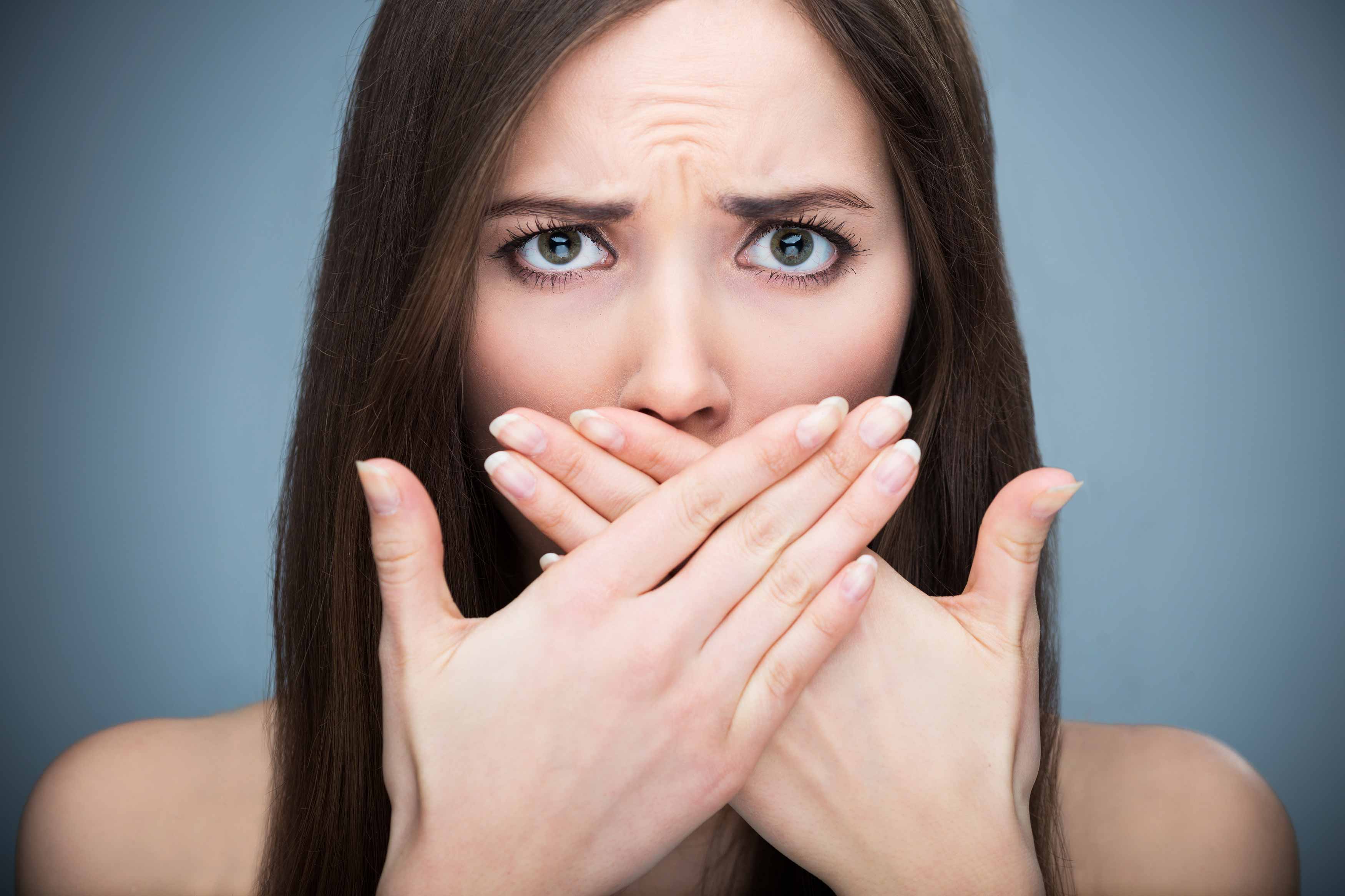 A photo of an embarassed lady covering her mouth because of bad breath and gum disease