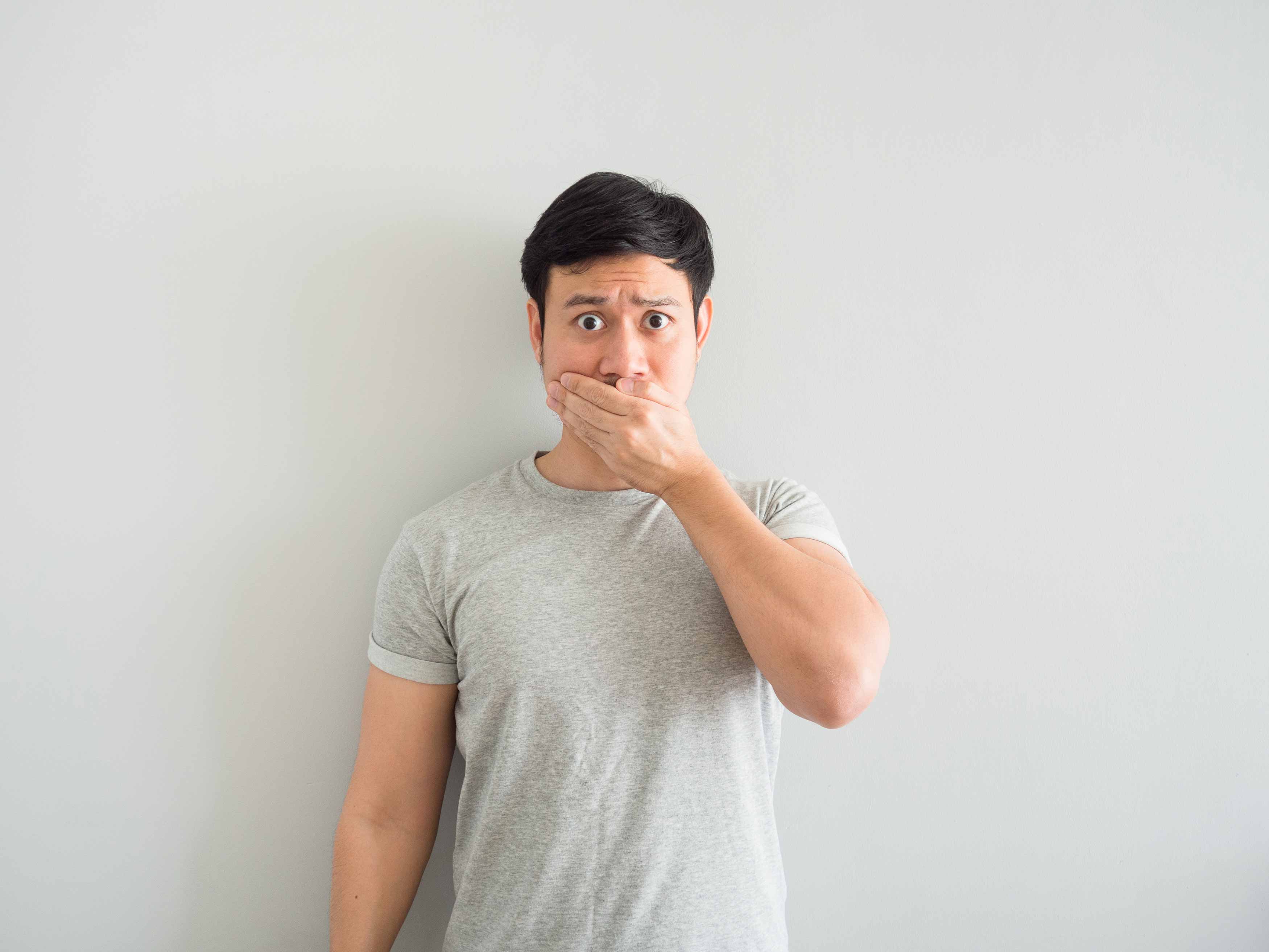 midbody photo of a male covering his mouth with his left hand because of he is embarassed by his bad breath