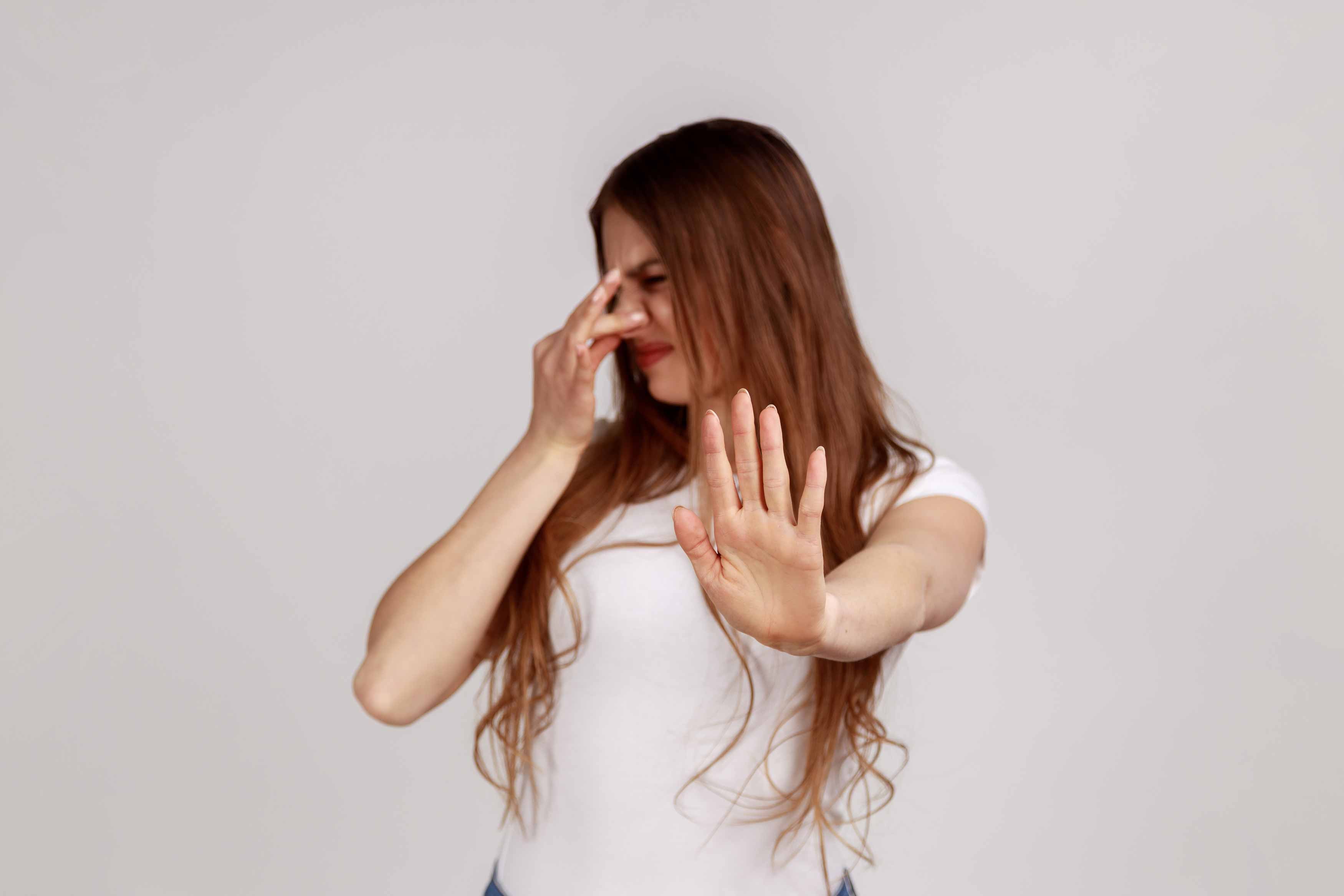 midbody photo of a young lady pinching her nose to stop smeeling and putting her other hand up to stop you from coming closer. indicating that there is a bad smell