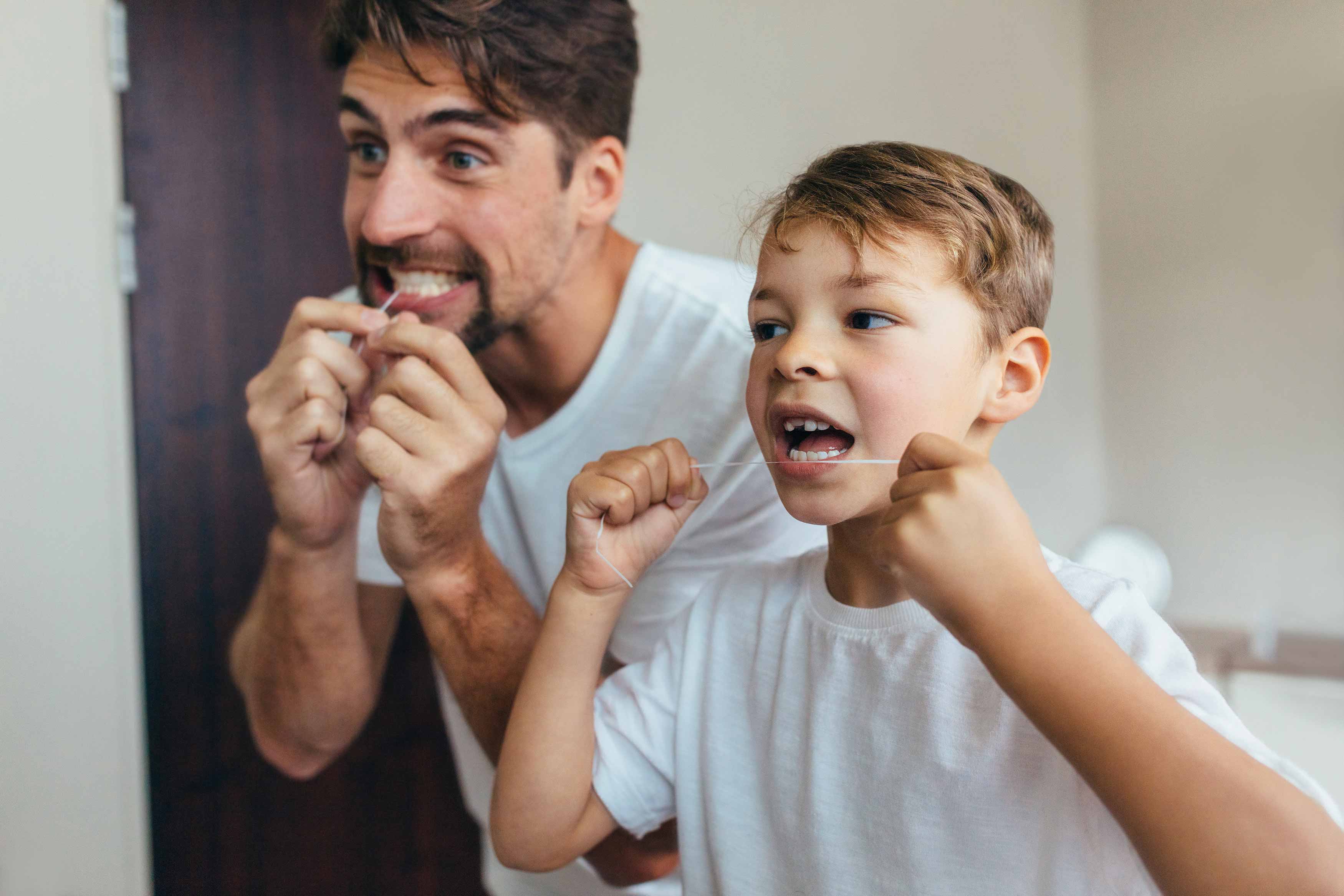 A photo of a father and son flossing their teeth together