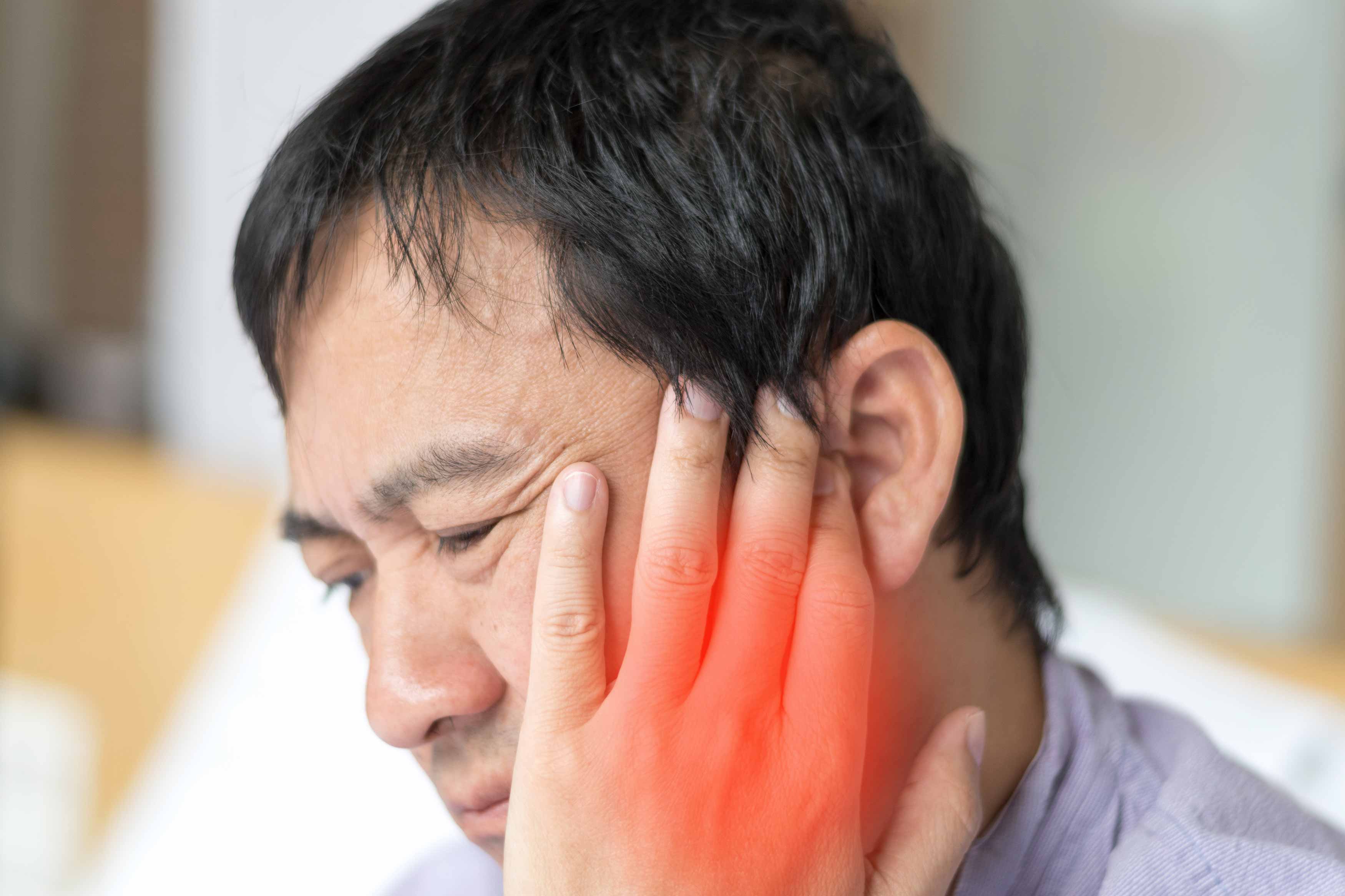 Photo of a male holding his left temple with his left hand because of a headache running up the side of his face