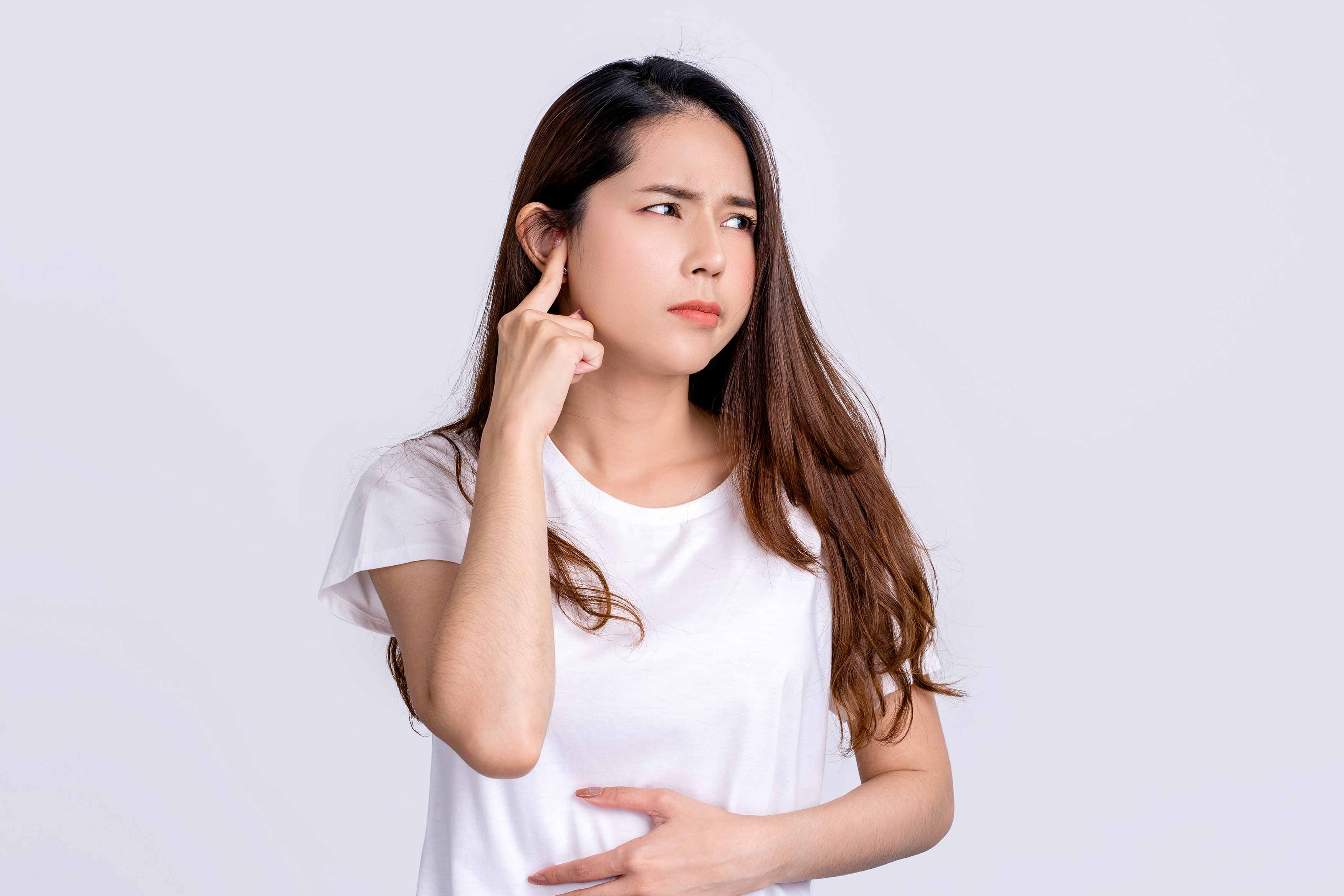Female putting her right index fingers over her right ear because of tinnitus
