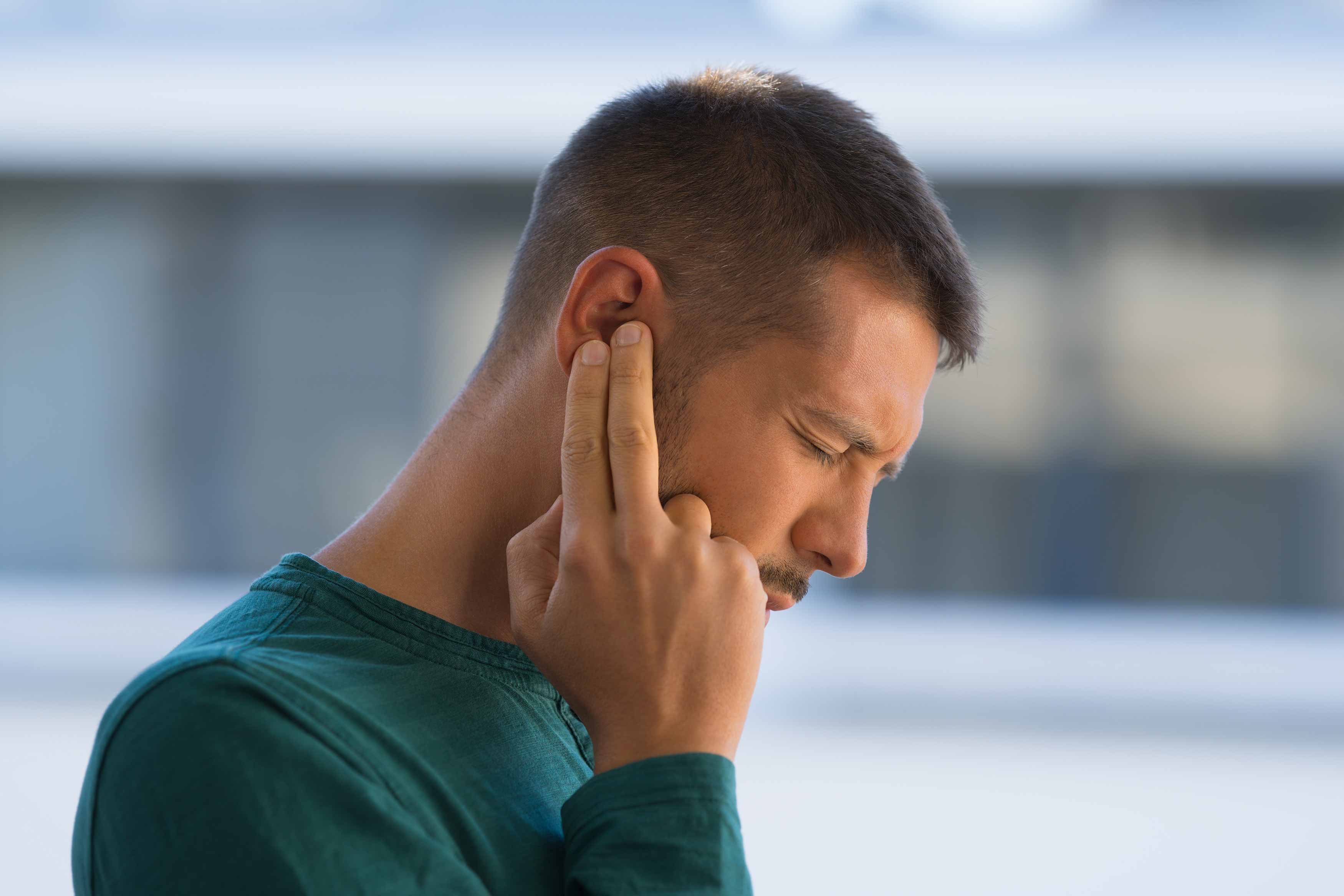 male putting his right index fingers over his right ear because of tinnitus