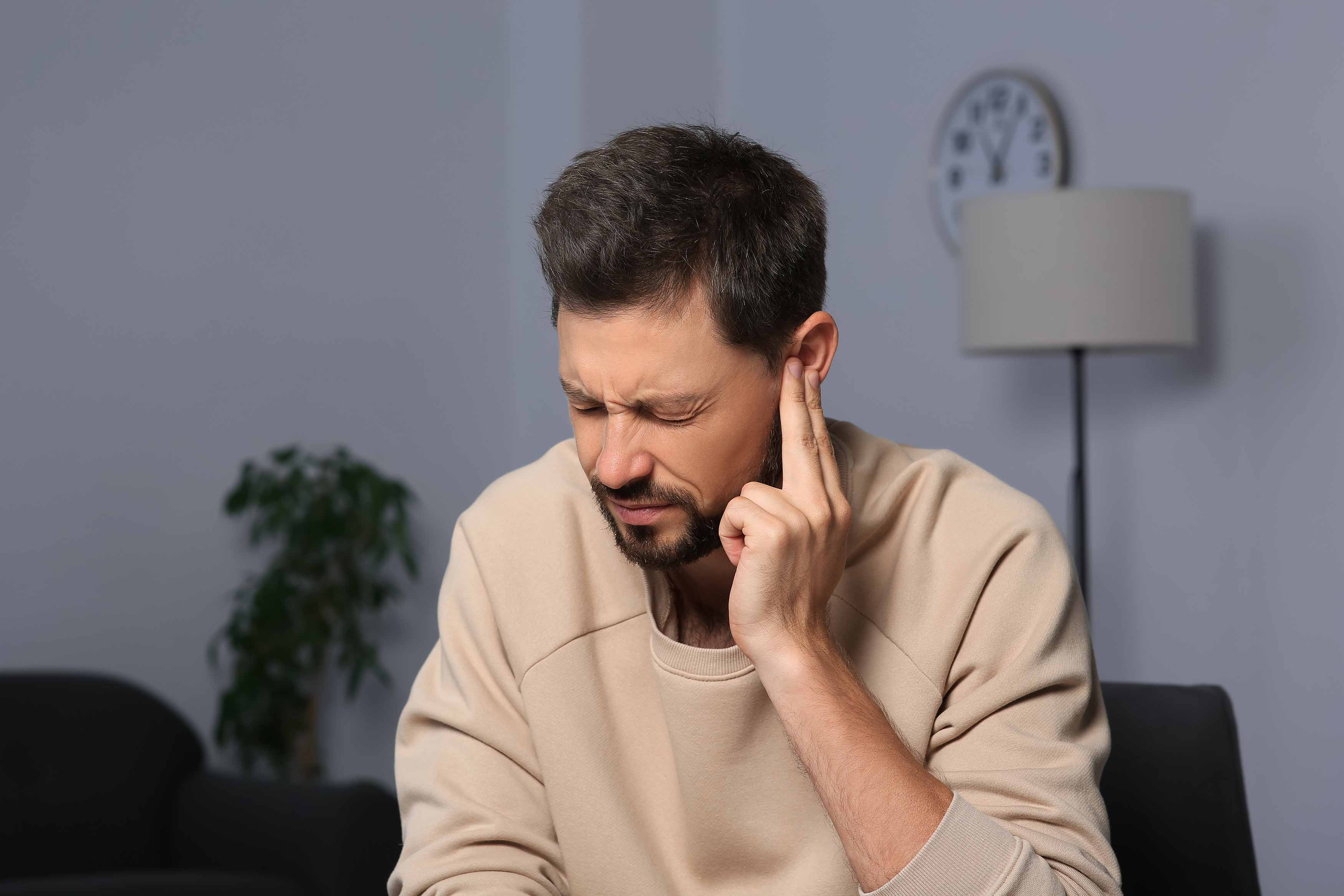 male putting his left index fingers over his left ear because of tinnitus