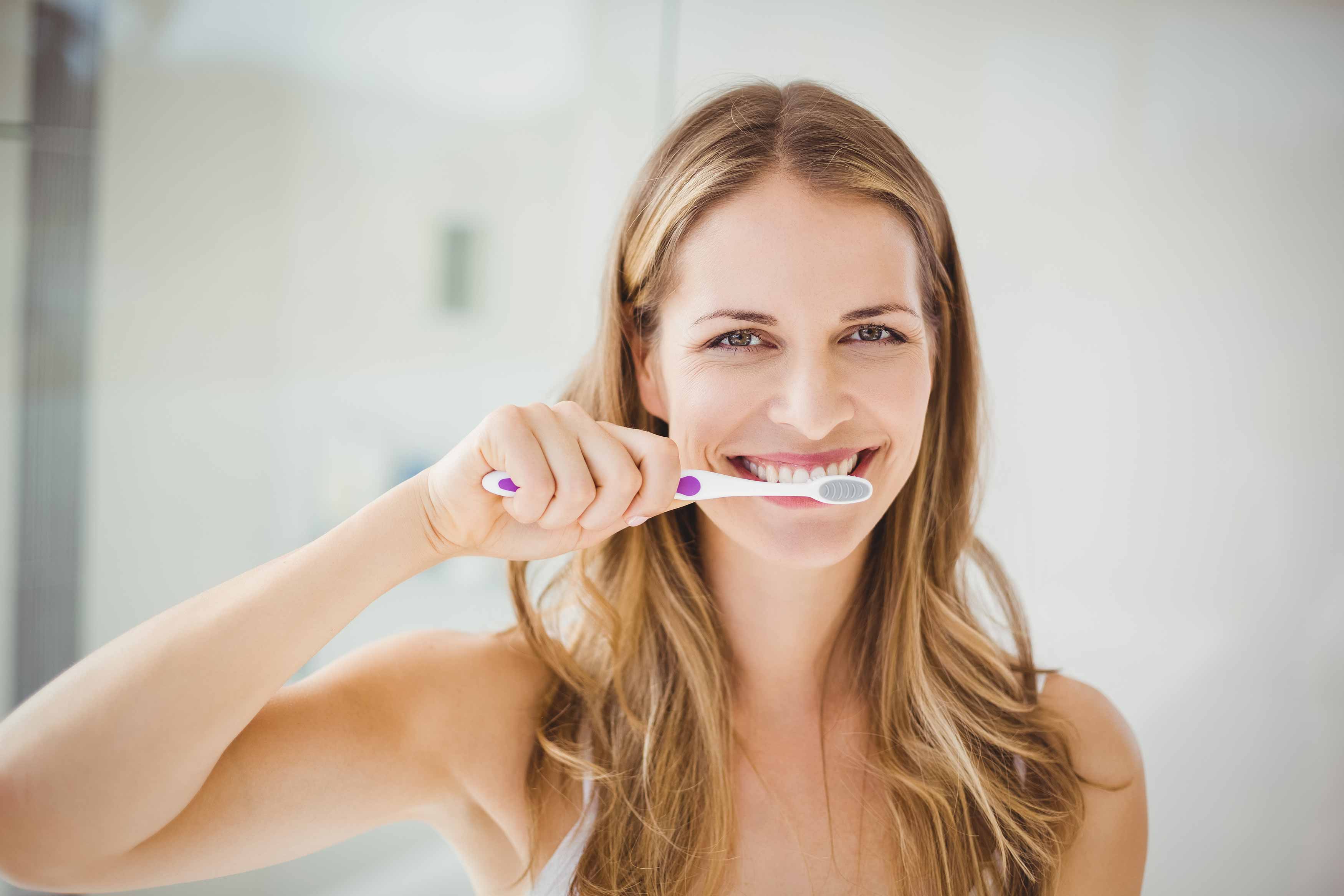 a photo of a lady brushing her teeth in front of a mirror