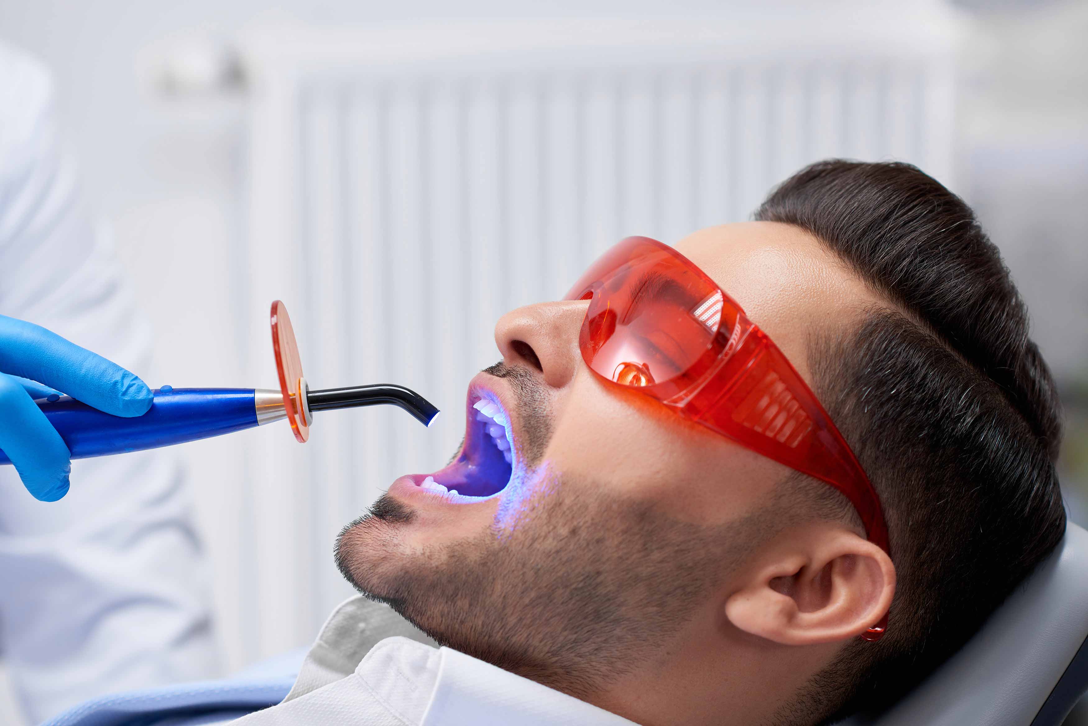 A photo of an UV light used to cure composite resin that is inside a patient's mouth , patient is wearing safety goggles. 