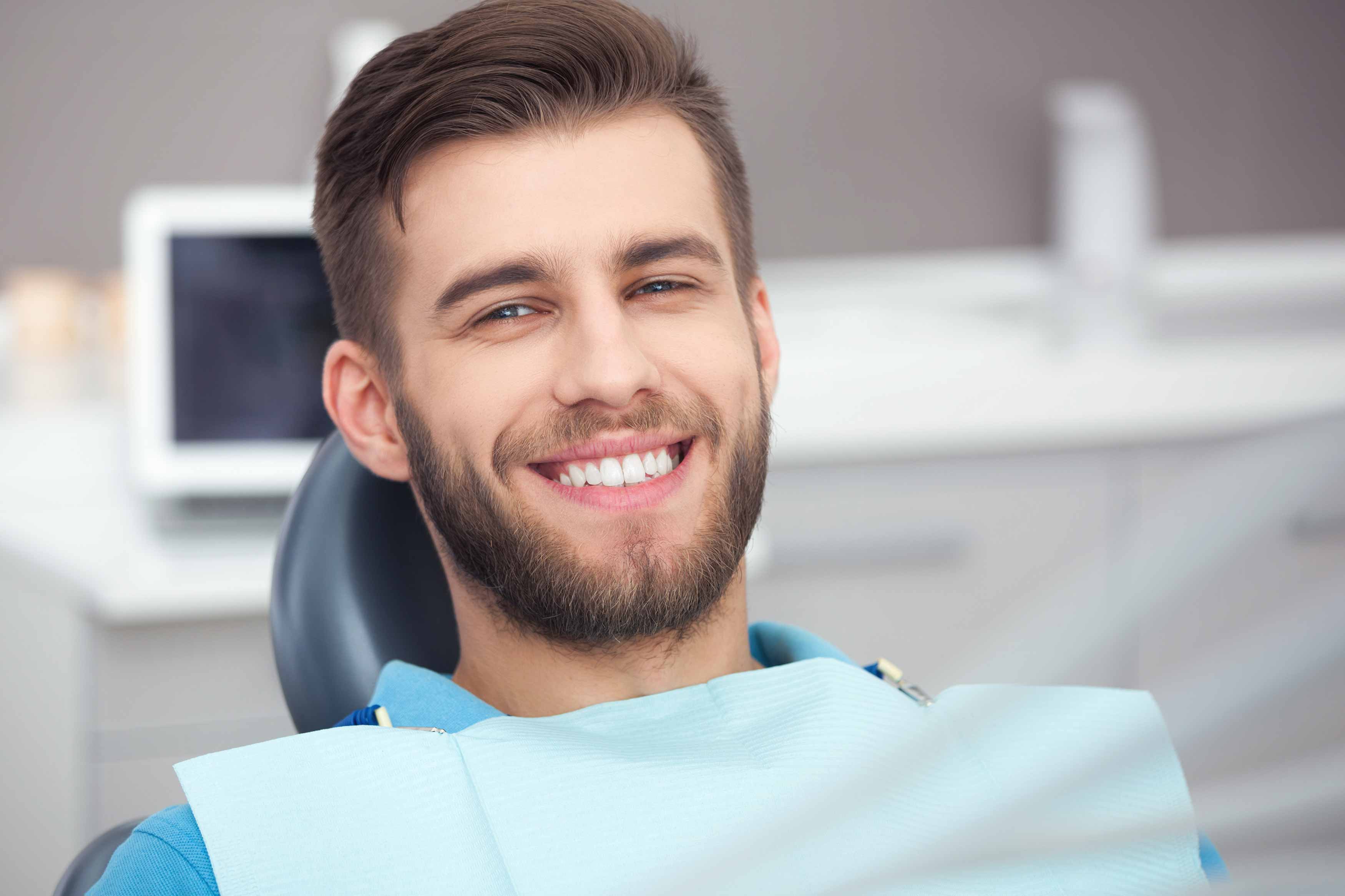 Photo of a young male sitting in the dental chair with a dental bib on smiling.