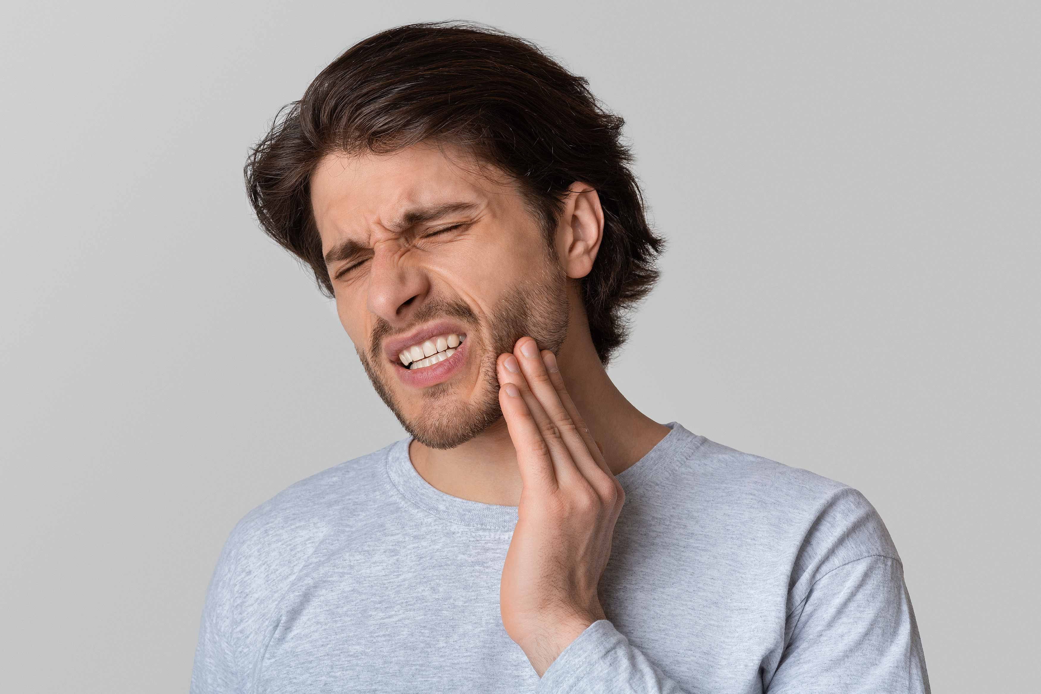 Photo of a person holding his L face showing grimace, possibly from a toothache