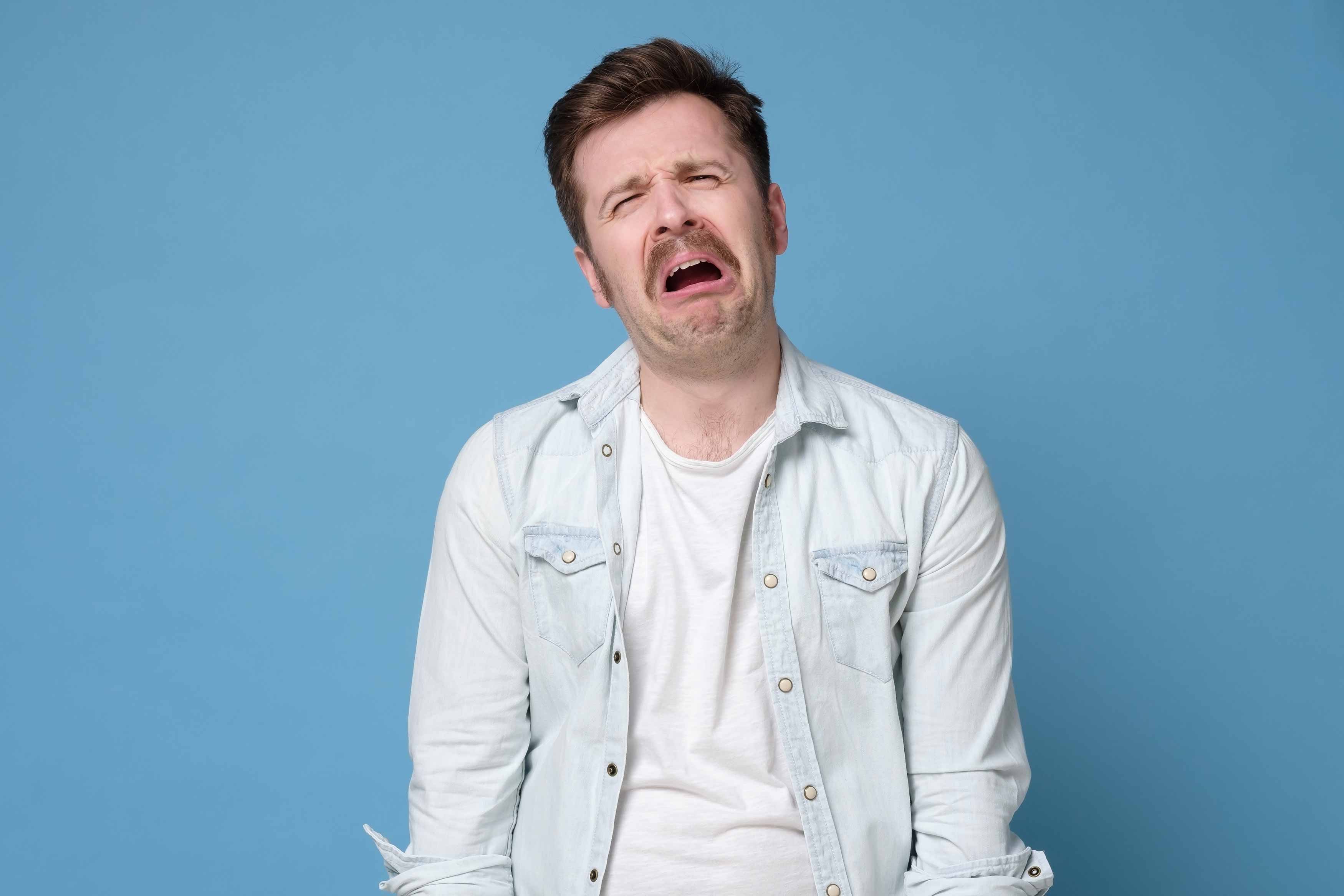 Photo of a grown male with a grimaced face indicating that is he is pain. 