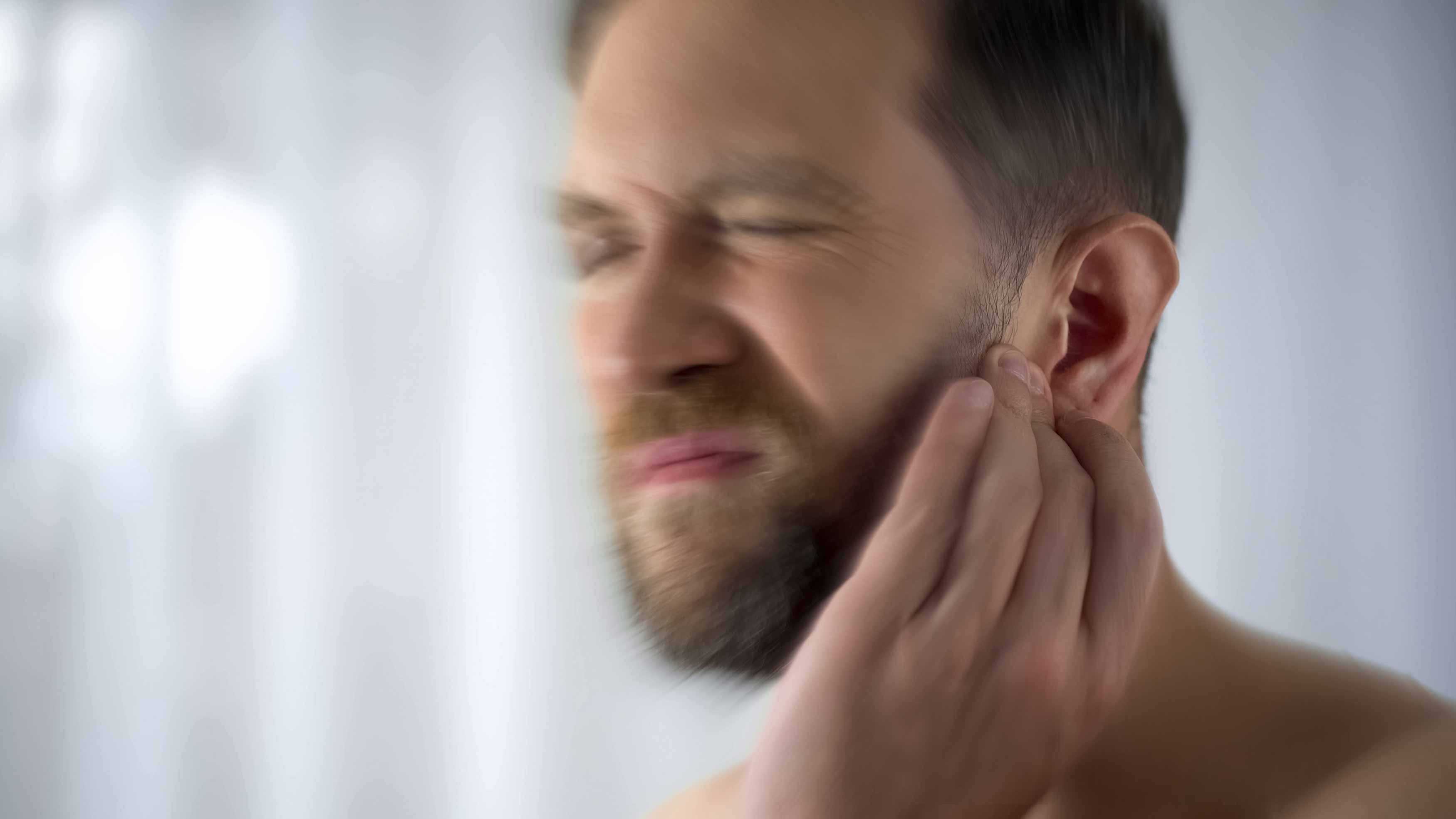 Photo of a male holding his left temple with his left hand because of a headache running up the side of her left jaw