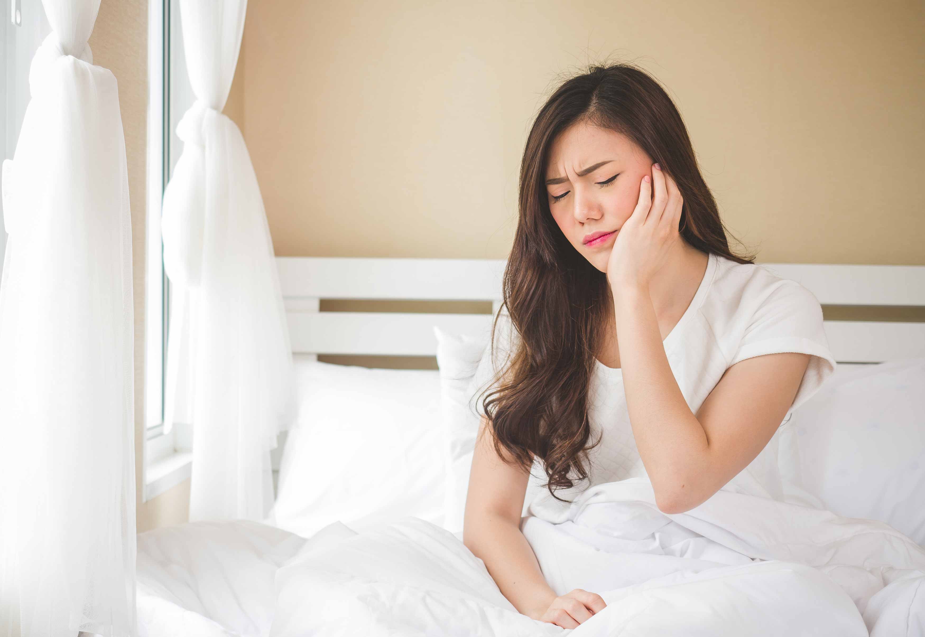 Female holding her left jaw in grimace because of her jaw pain