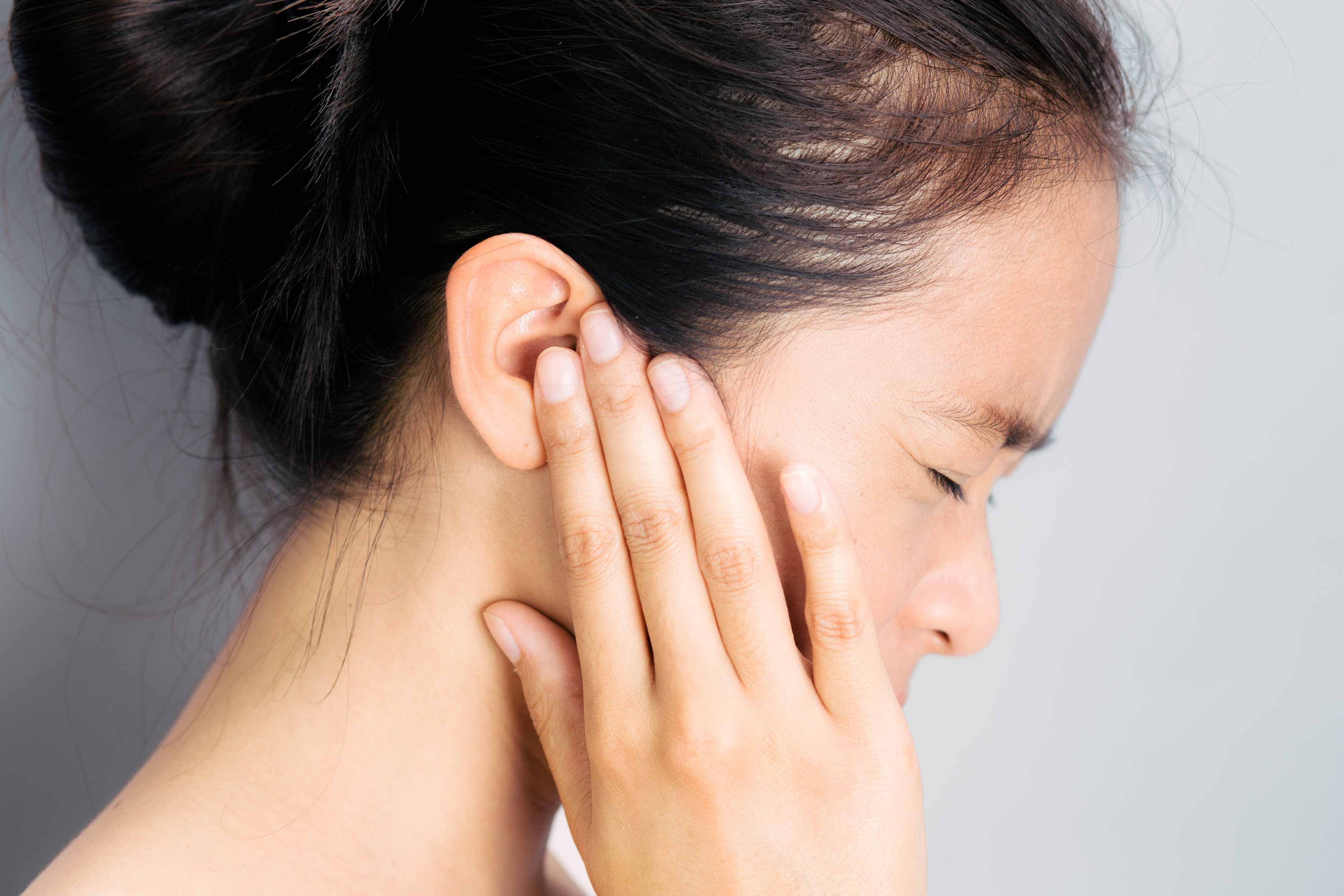 A female putting her fingers in both ears and squinting her eyes, trying to stop hearing sounds