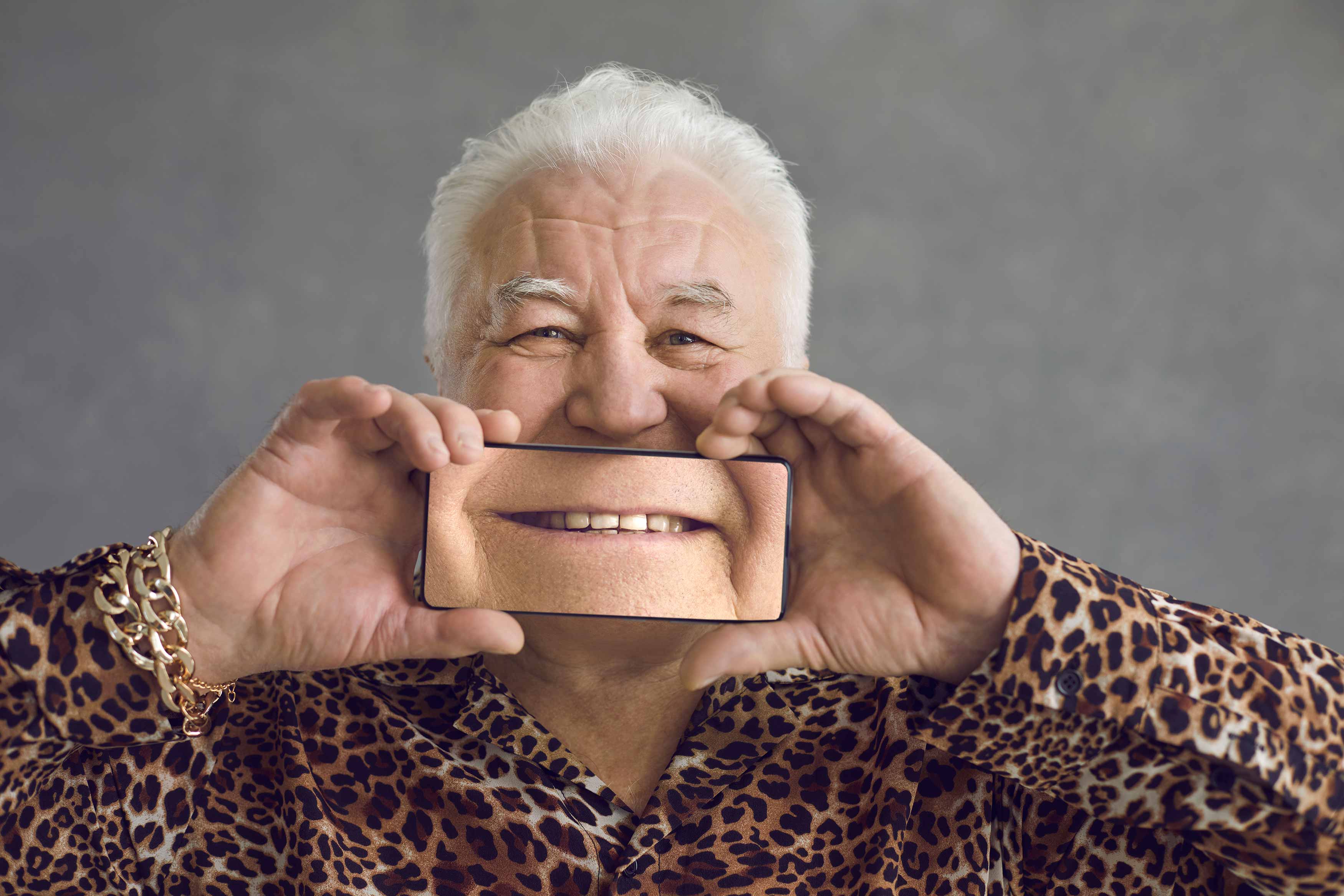 An elderman holding up a blown up photo of his teeth showing off his dentures