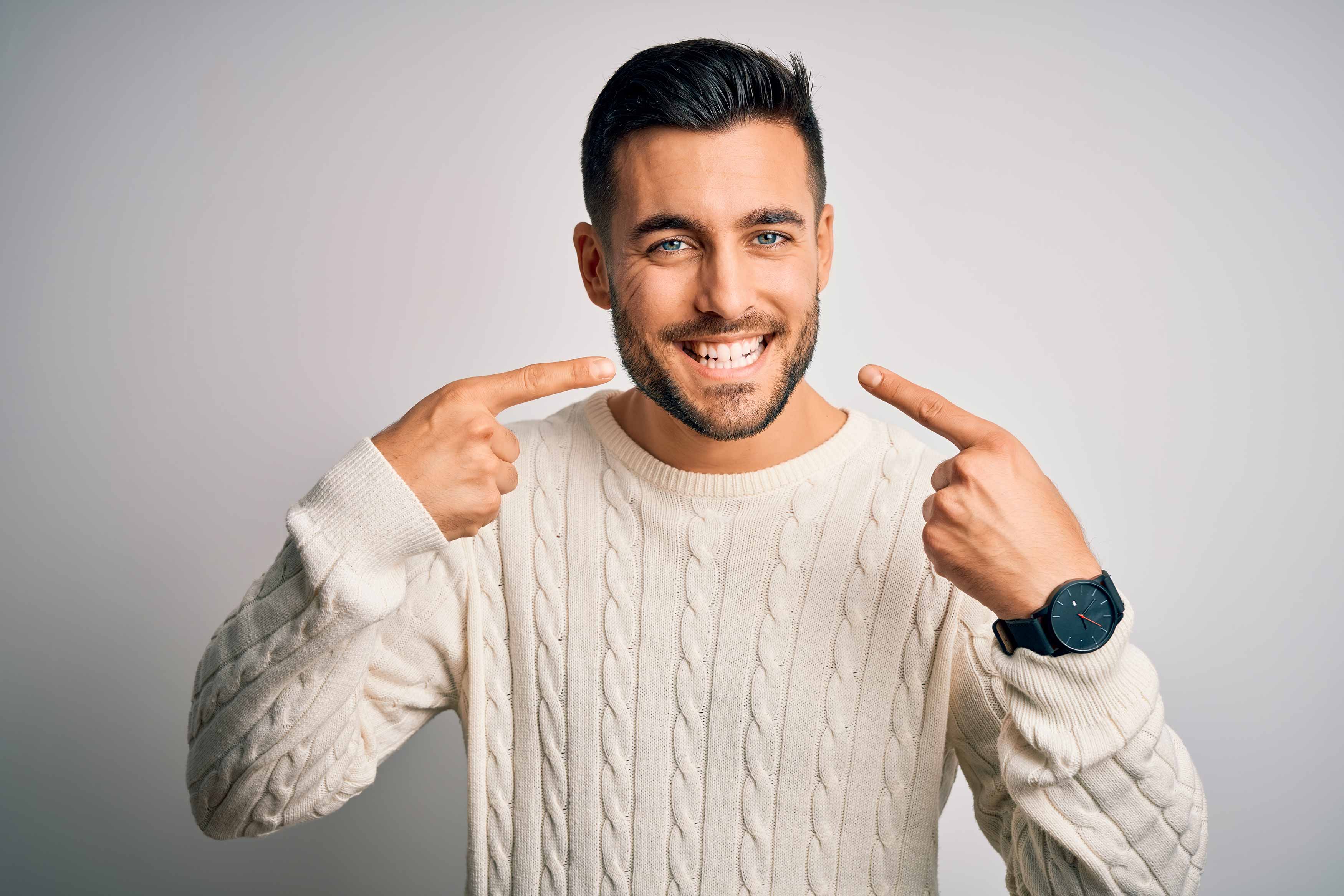 A photo of a man pointing at his teeth being very happy with his smile