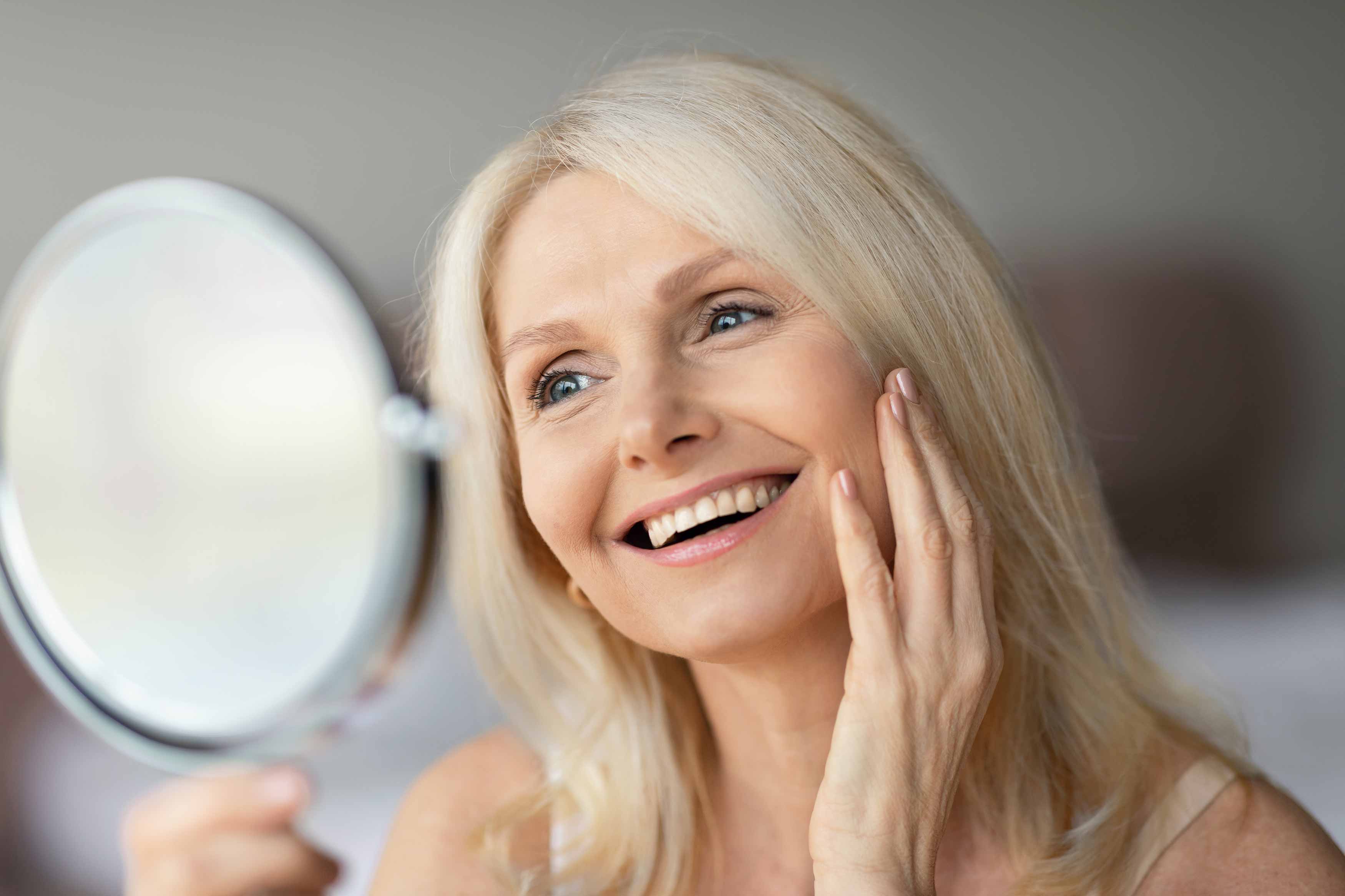 A photo of an elderly lady looking at her new smile through her mirror