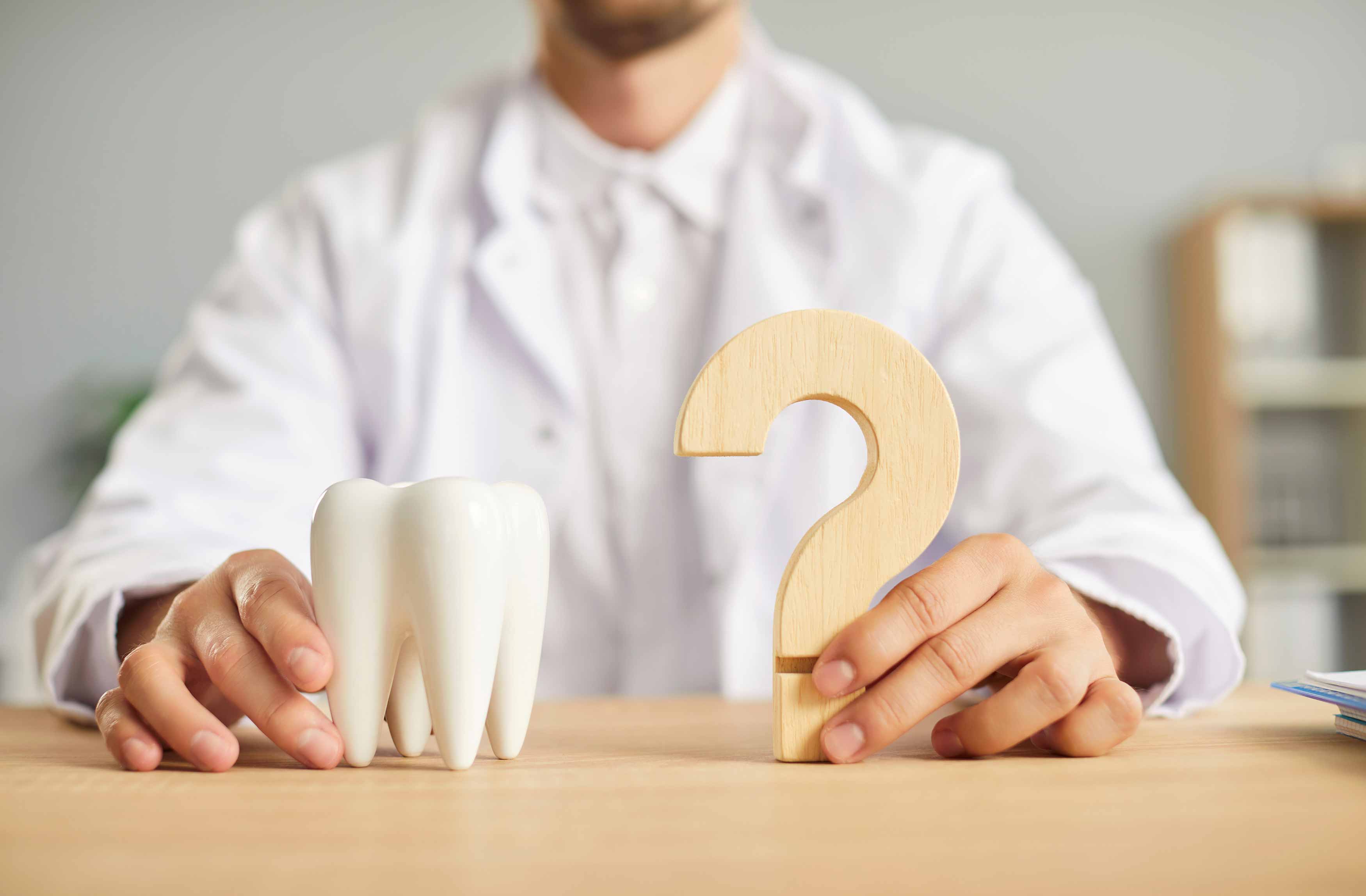 A photo of a men holding a tooth model in his right and a question mark on his left