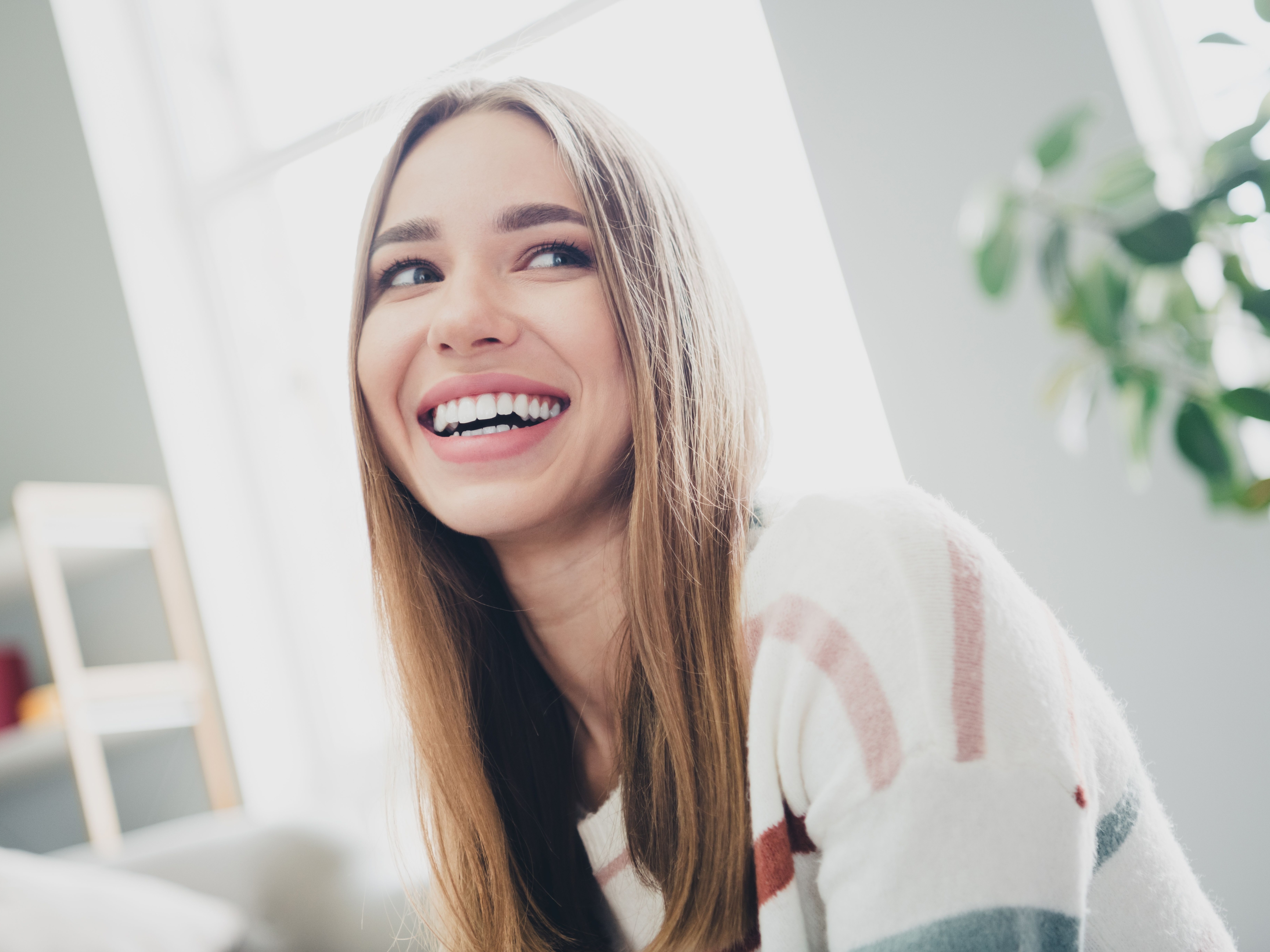Young woman enjoying a relaxing day at home in natural daylight, smiling in the living room, capturing moments of joy and tranquility.