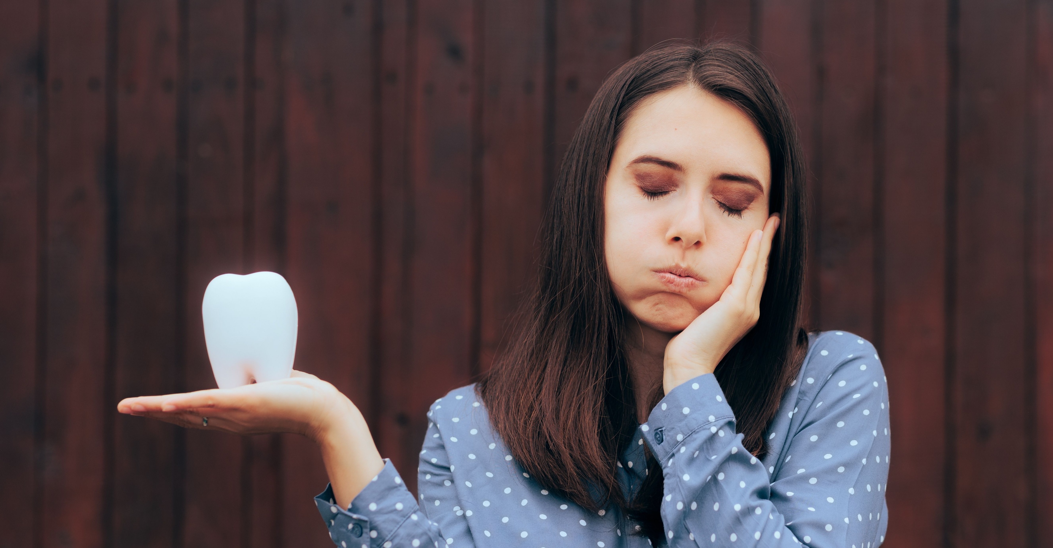  Unhappy Woman Suffering a Toothache Holding a Molar. Patient feeling pain after wisdom tooth infection 
