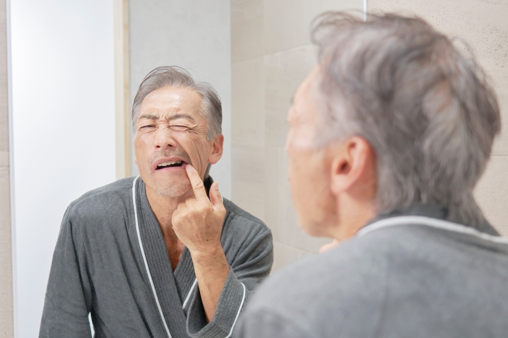 Elderly Asian man checking his teeth in the mirror