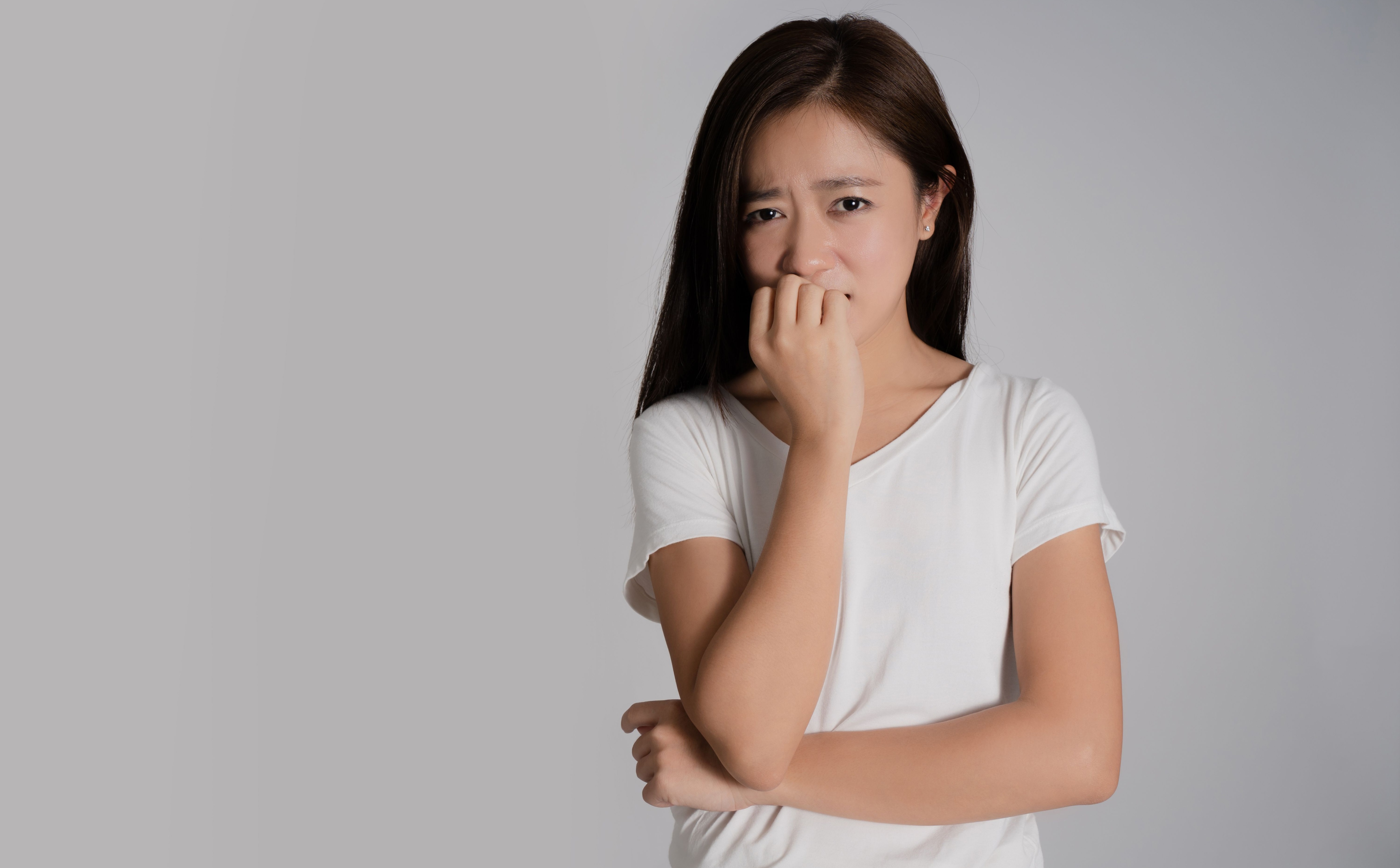 Asian woman is worried. She is standing thinking about something. Isolated on background.