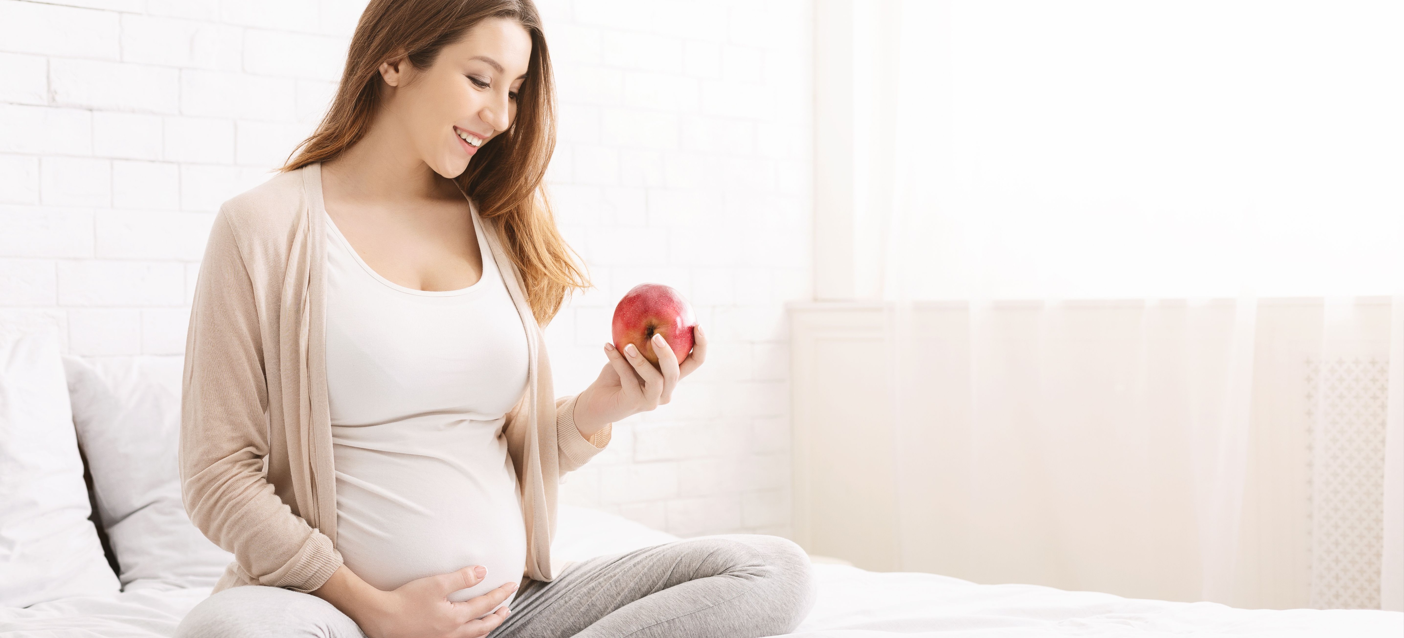 Dental care. Young pregnant woman enjoying fresh apple in bed, empty space