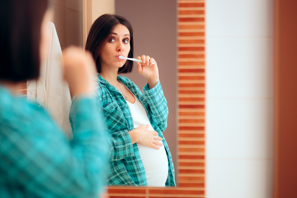 Pregnant Woman Wearing Pajamas Brushing her Teeth. Mother to be being careful with oral hygiene during pregnancy