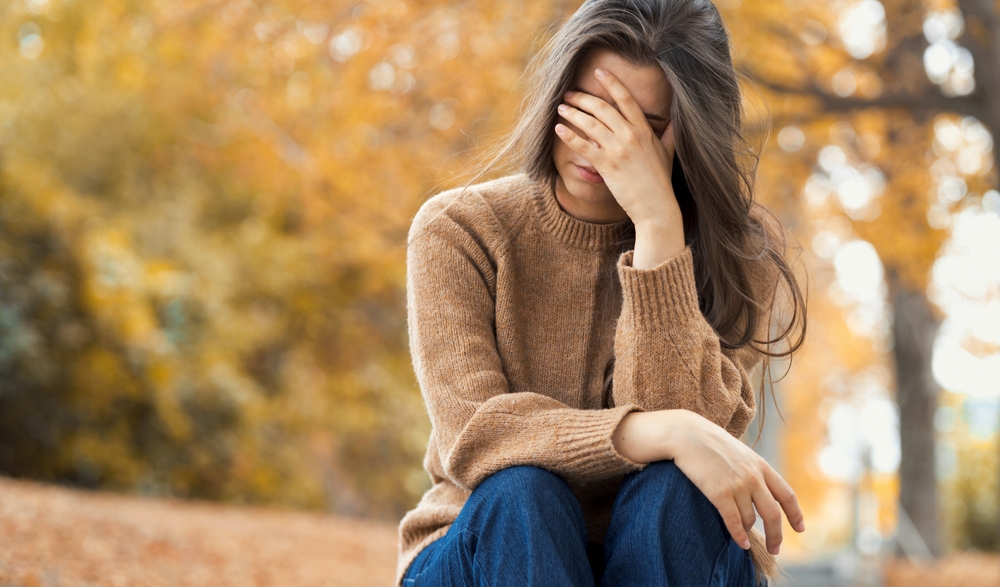 Closeup faceless upset woman has mental health problems. Melancholic girl covered her face with her hands sitting on the steps in the autumn park. Autumn depression, melancholy and blues.
