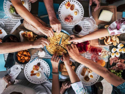 Food in the middle of a table and hands reaching in to take food off a plate