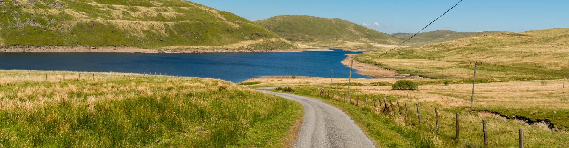 Country lane leading to a lake surrounded by green hills near Aberystwyth, perfect for spring walks.