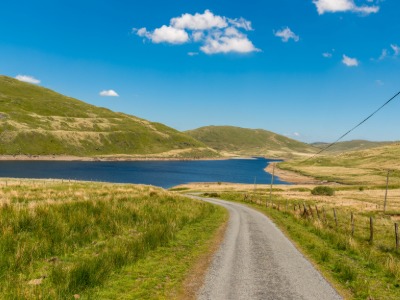 Country lane leading to a lake surrounded by green hills near Aberystwyth, perfect for spring walks.