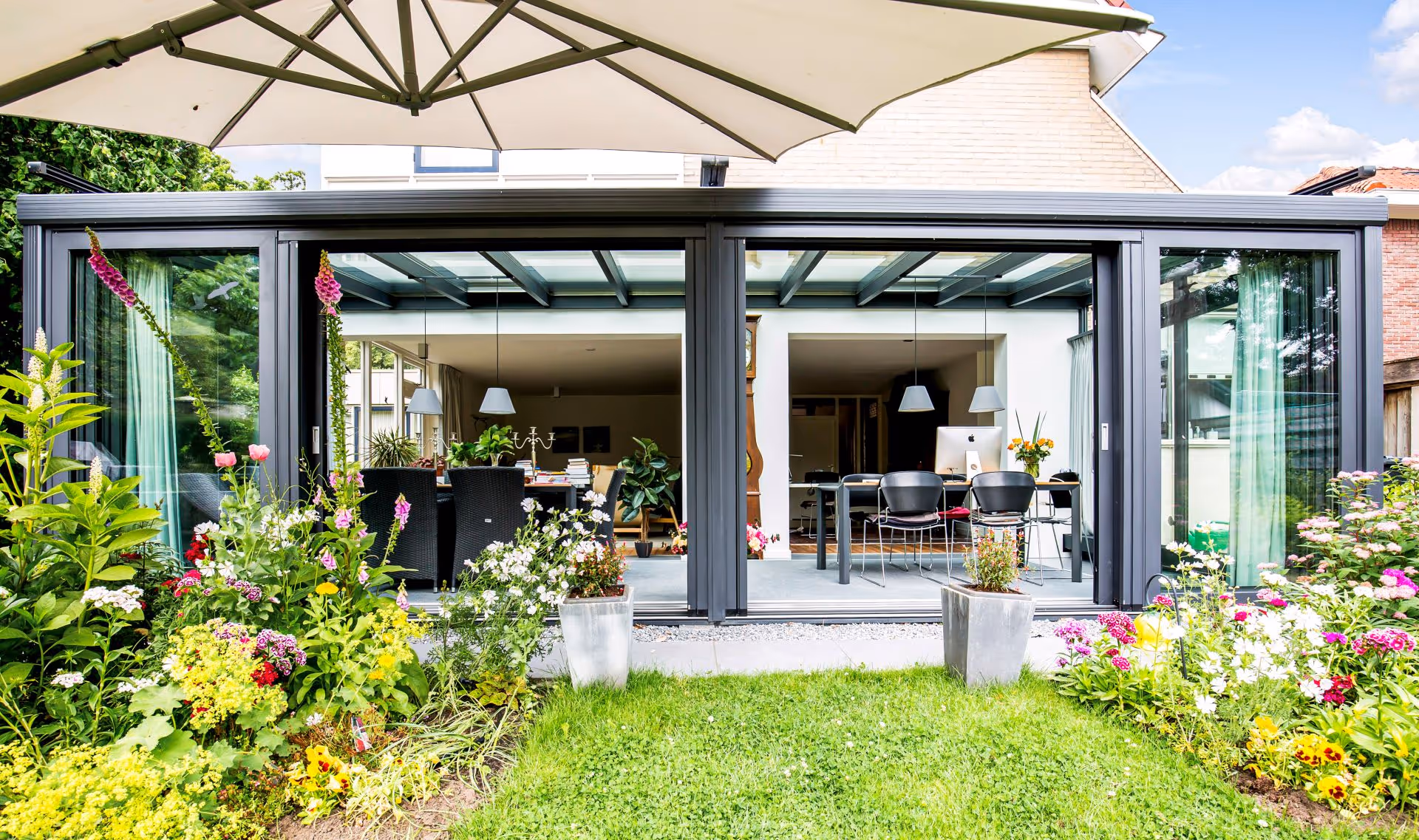 Luxe moderne serre met glazen dak en schuifpuien, geïntegreerd in een groene tuin