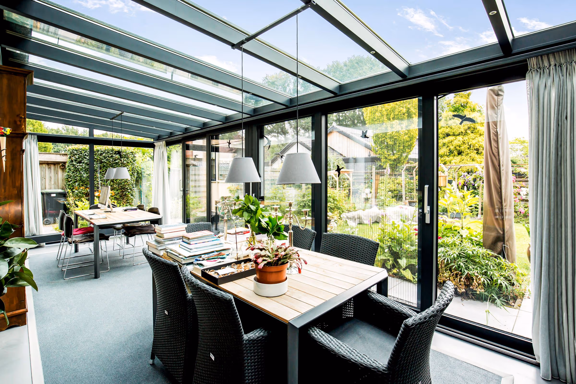 Serre interieur met glazen dak en schuifdeuren, ingericht met eettafel en zicht op de tuin