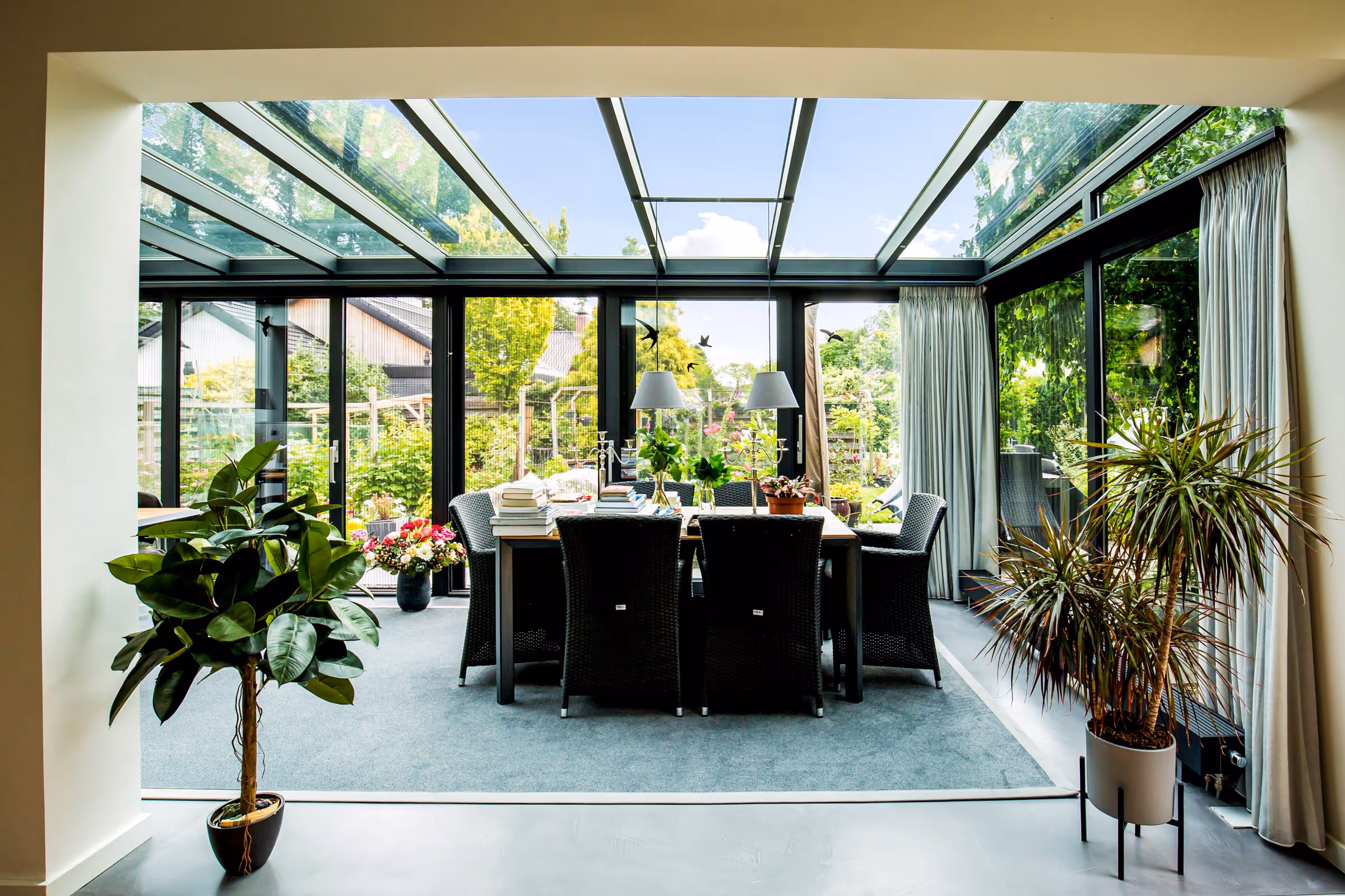 Ruime tuinkamer met glazen dak en grote raampartijen, voorzien van eettafel en veel daglicht