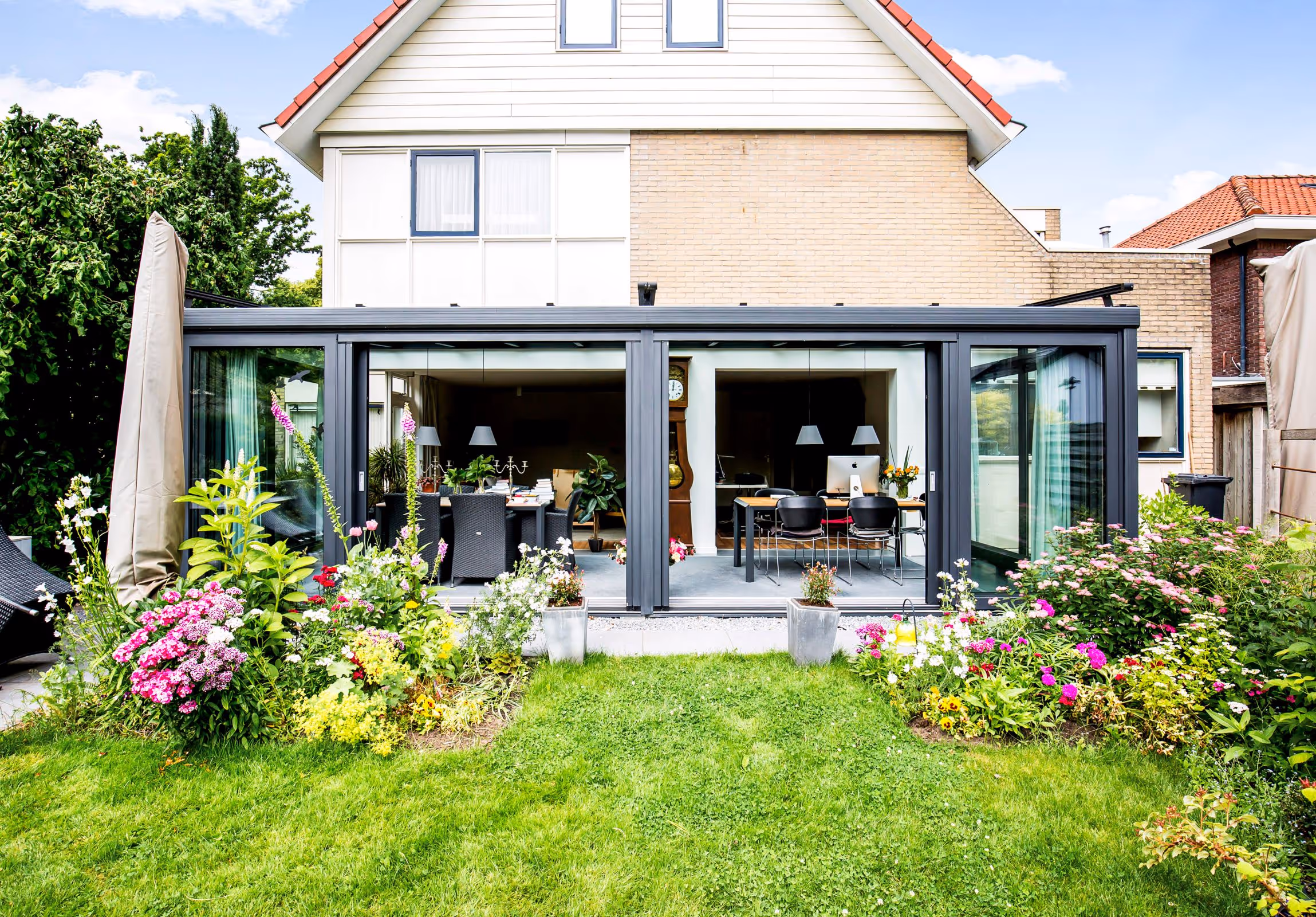 Achteraanzicht van een woning met serre aanbouw en open schuifpuien naar de tuin
