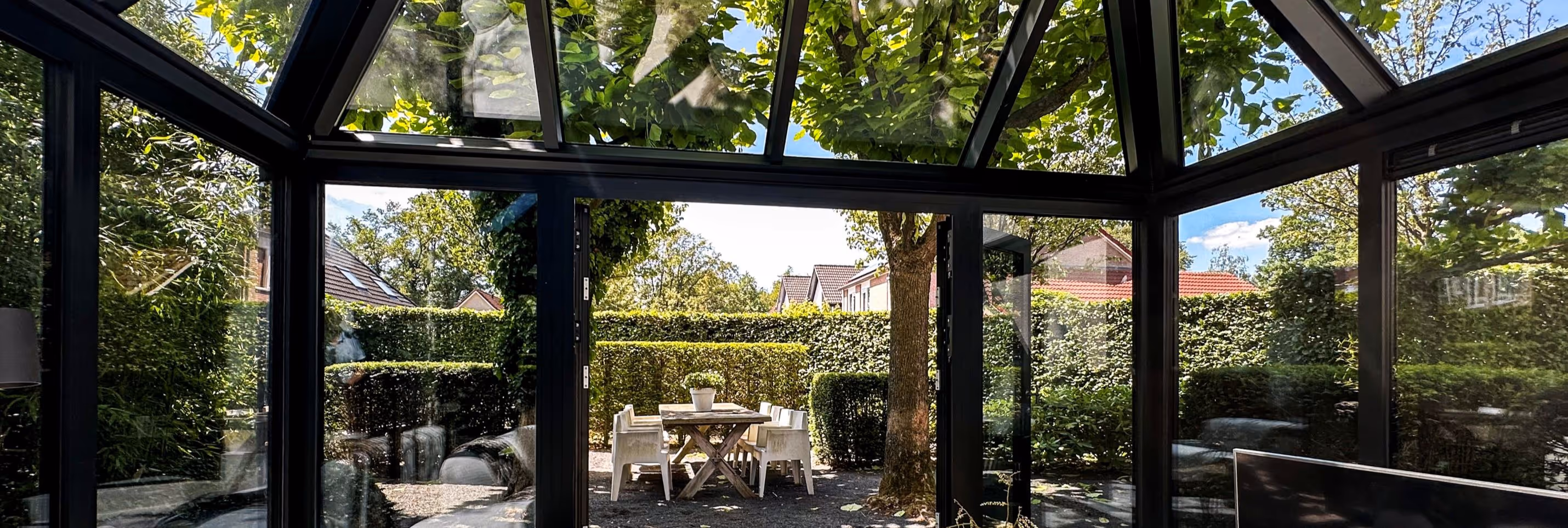 Ruime serre met glazen dak en wanden, met uitzicht op een tuin en terras