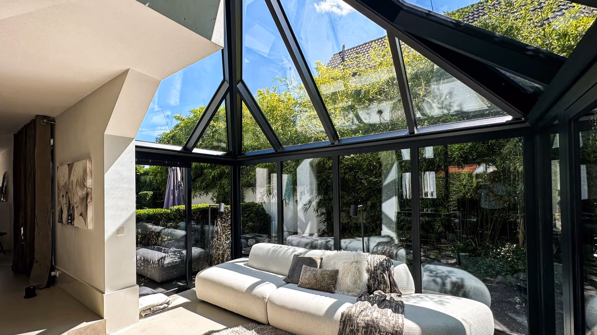 Luxe serre woonkamer met glazen dak en open deuren naar een groene tuin