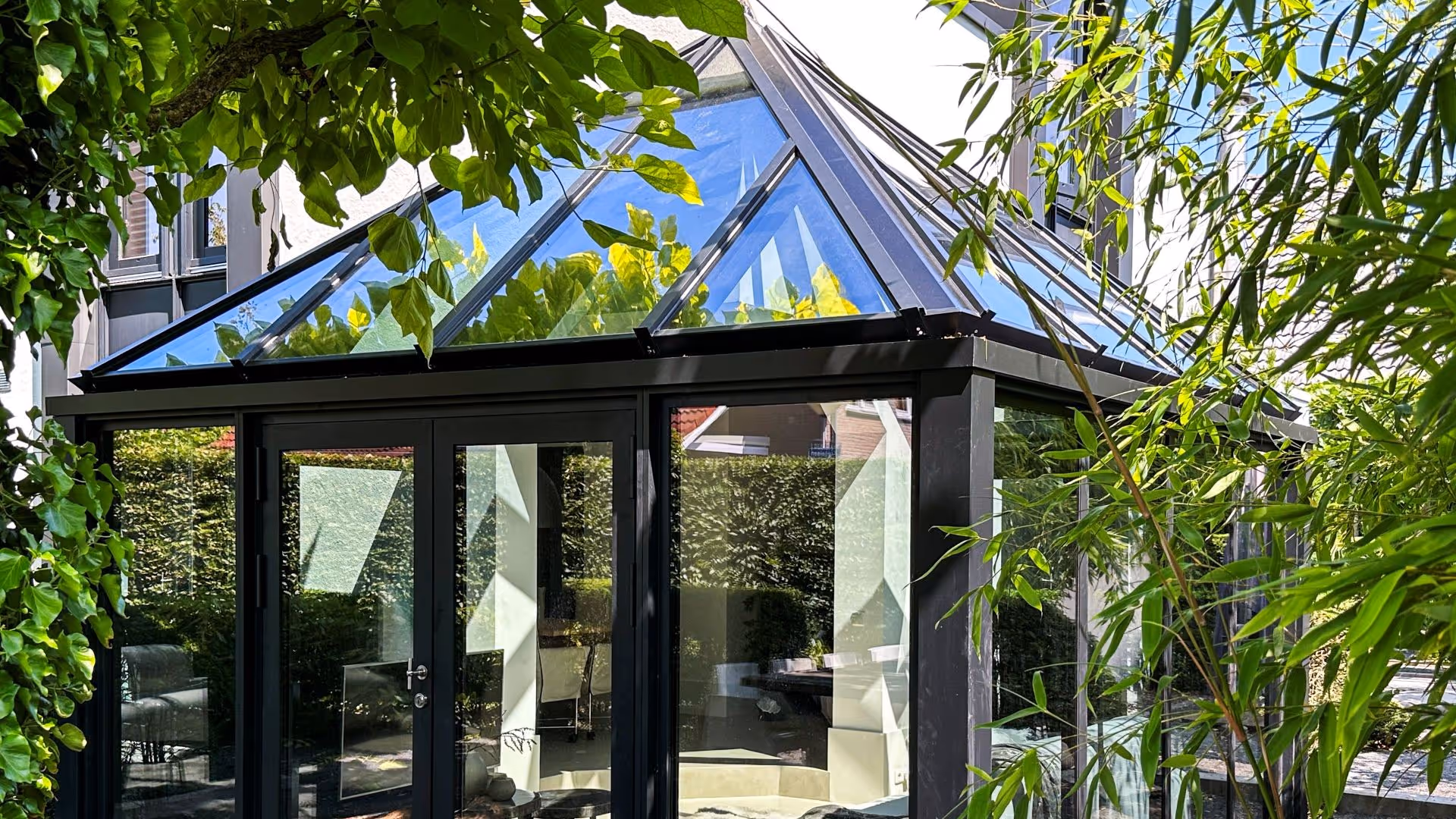 Detail van een moderne aluminium serre met glazen dakconstructie en zwarte profielen in een tuinomgeving
