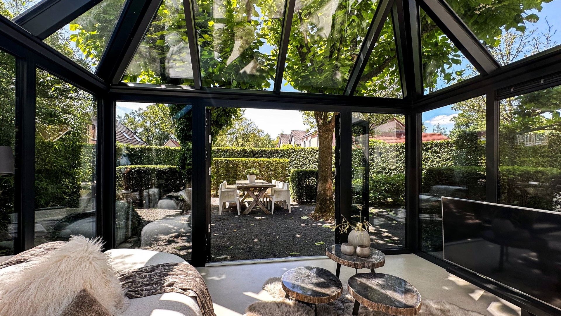 Moderne serre met glazen dak en zwarte kozijnen, met zicht op tuin en buitenruimte
