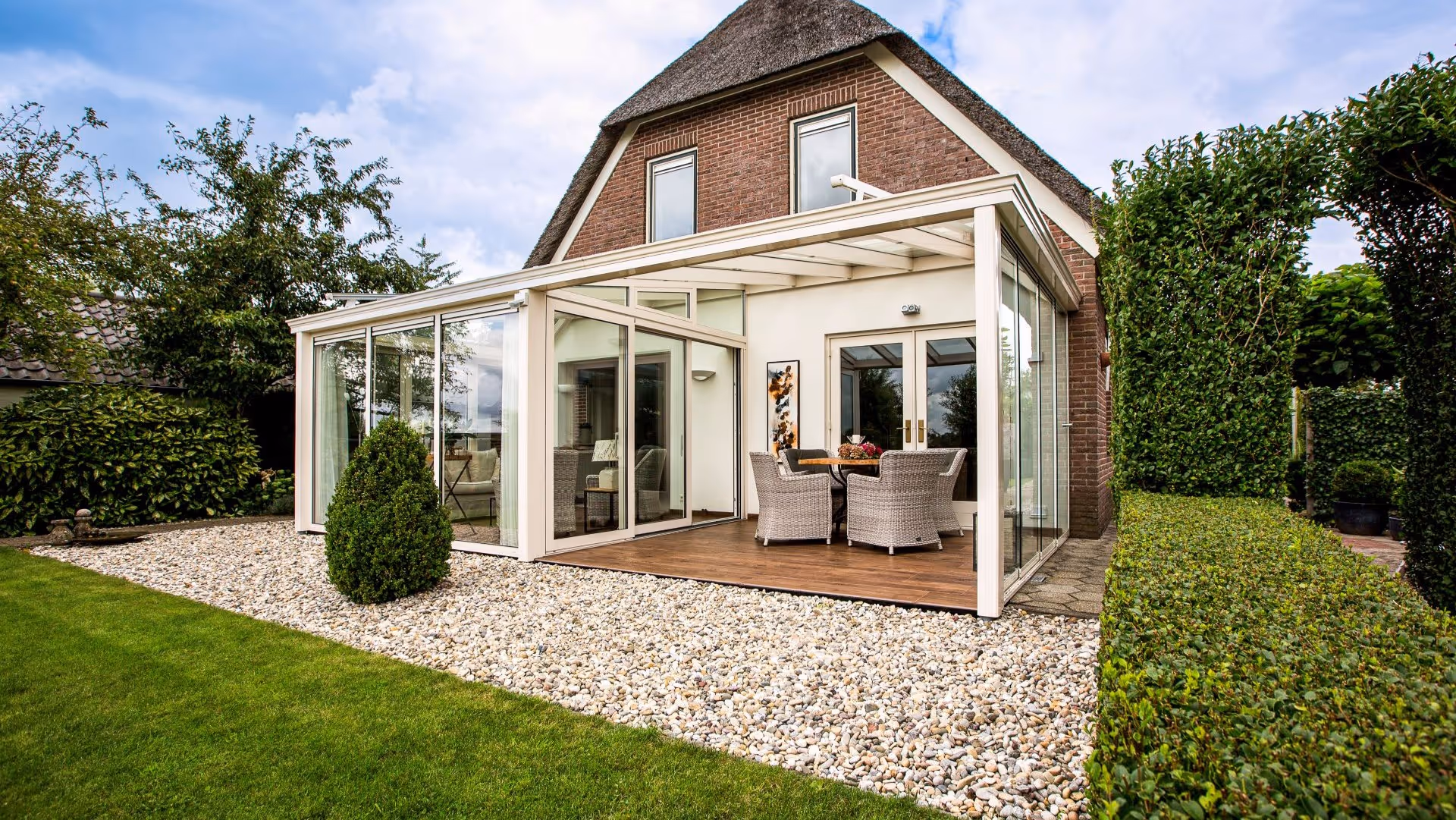 Witte aluminium serre aanbouw met glazen schuifwanden en overkapping naast een woning