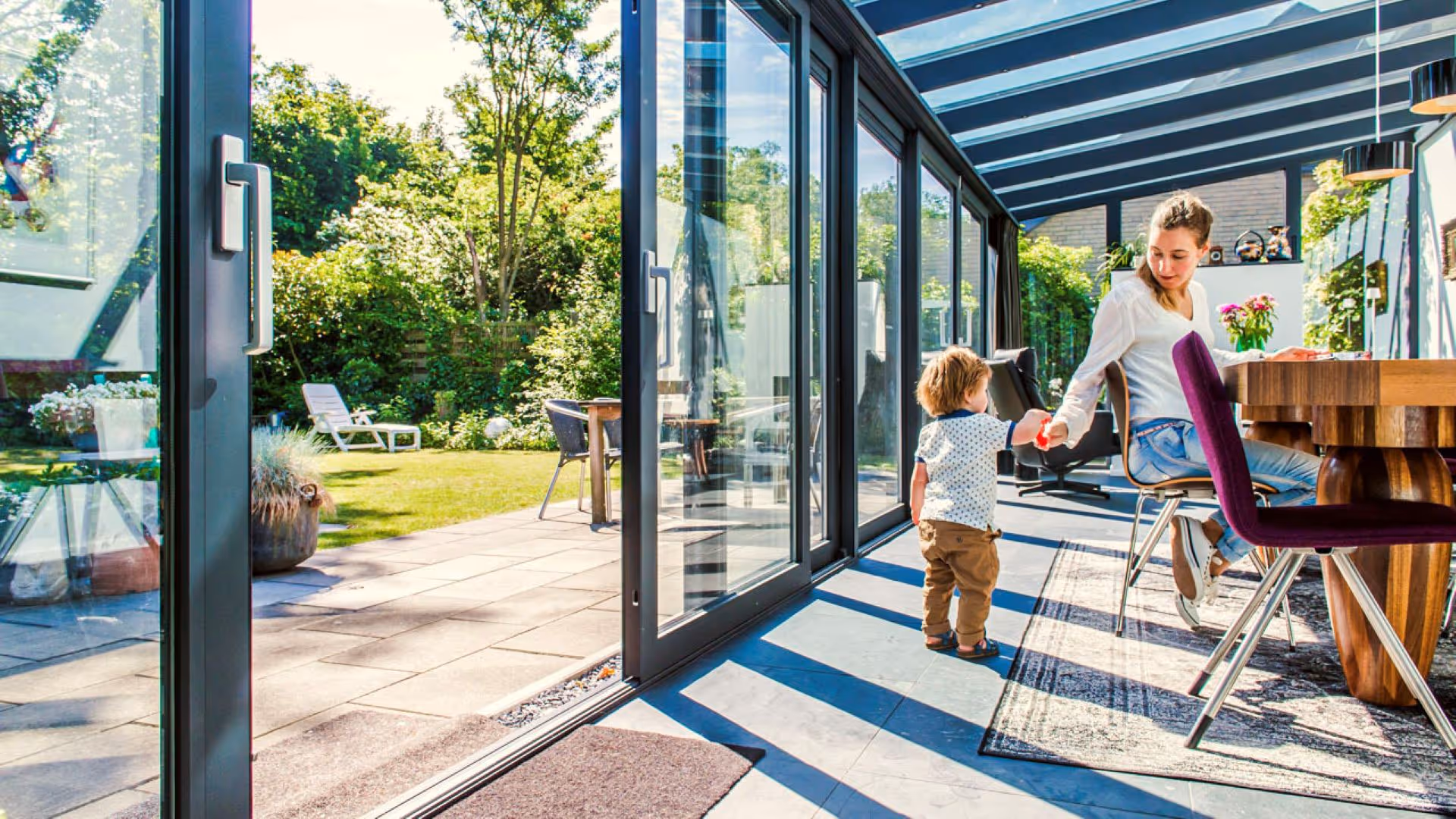 Lichte serre met glazen schuifpuien en open verbinding met de tuin