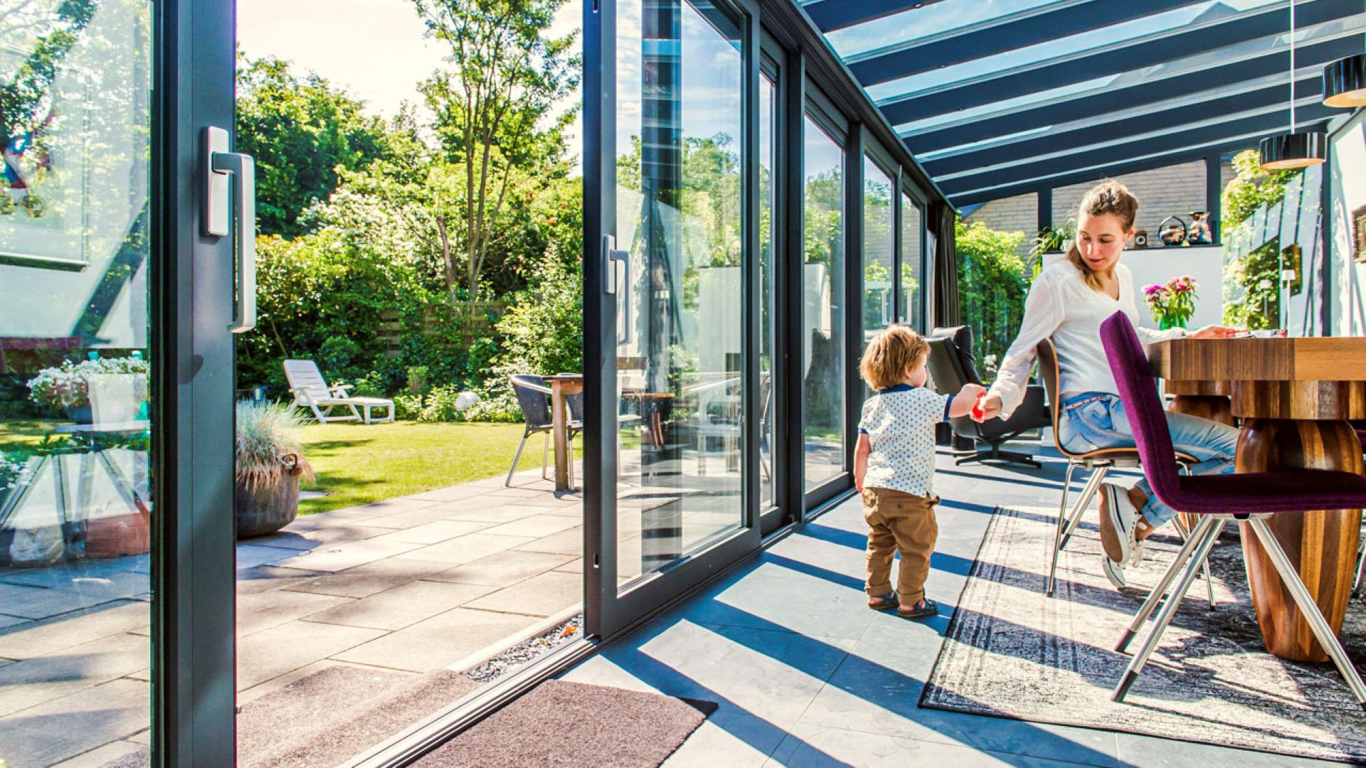 Lichte serre met glazen schuifpuien en open verbinding met de tuin