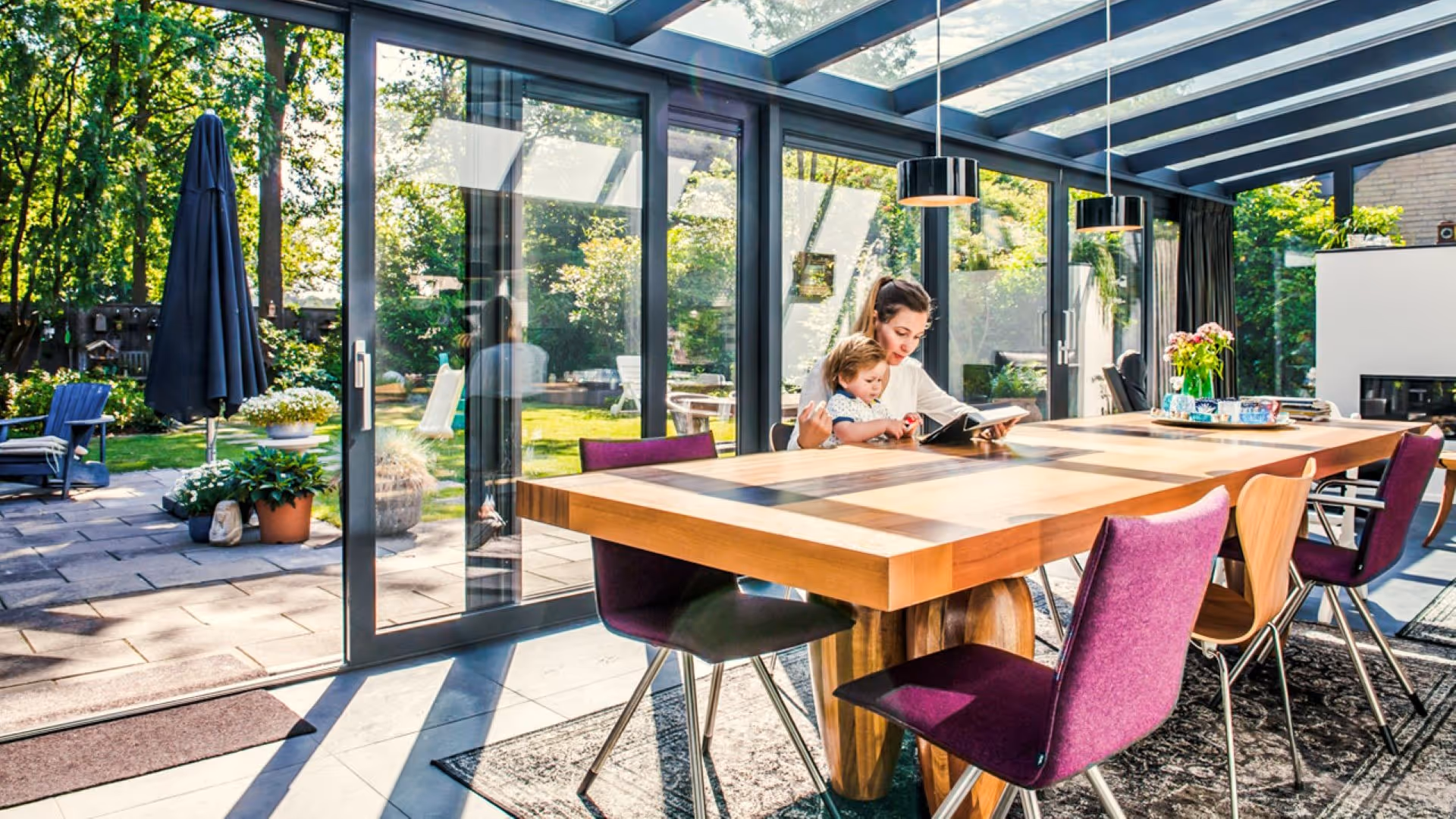 Ruime serre met houten eettafel, glazen dak en grote schuifpuien